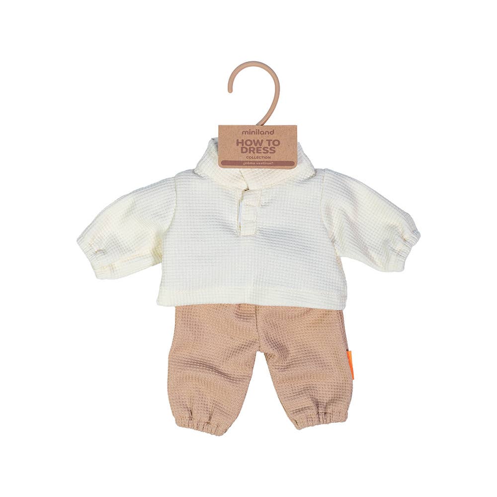 Baby outfit with white top and beige pants on a hanger against a white background