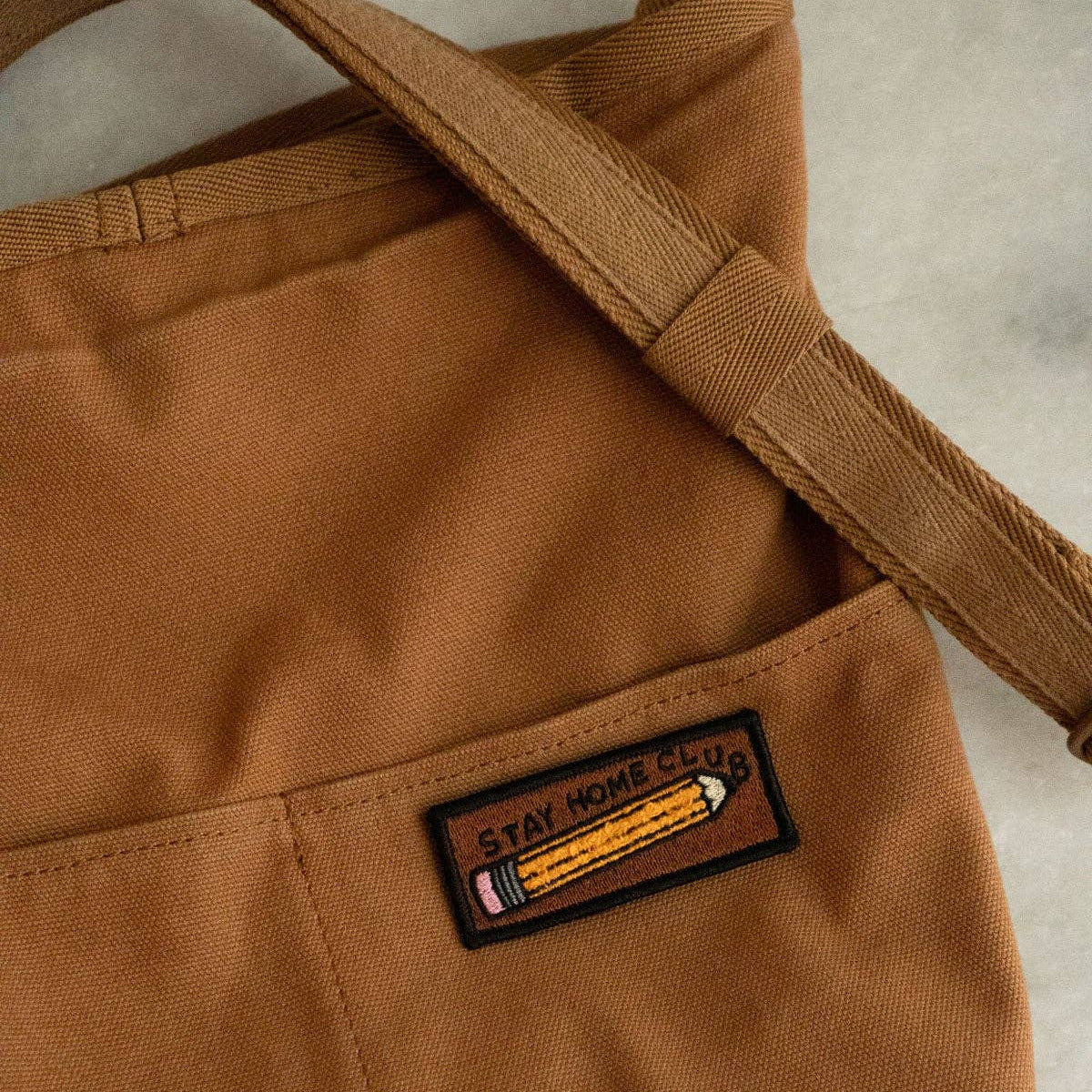 Brown bag with a patch featuring a pencil and text on a neutral background