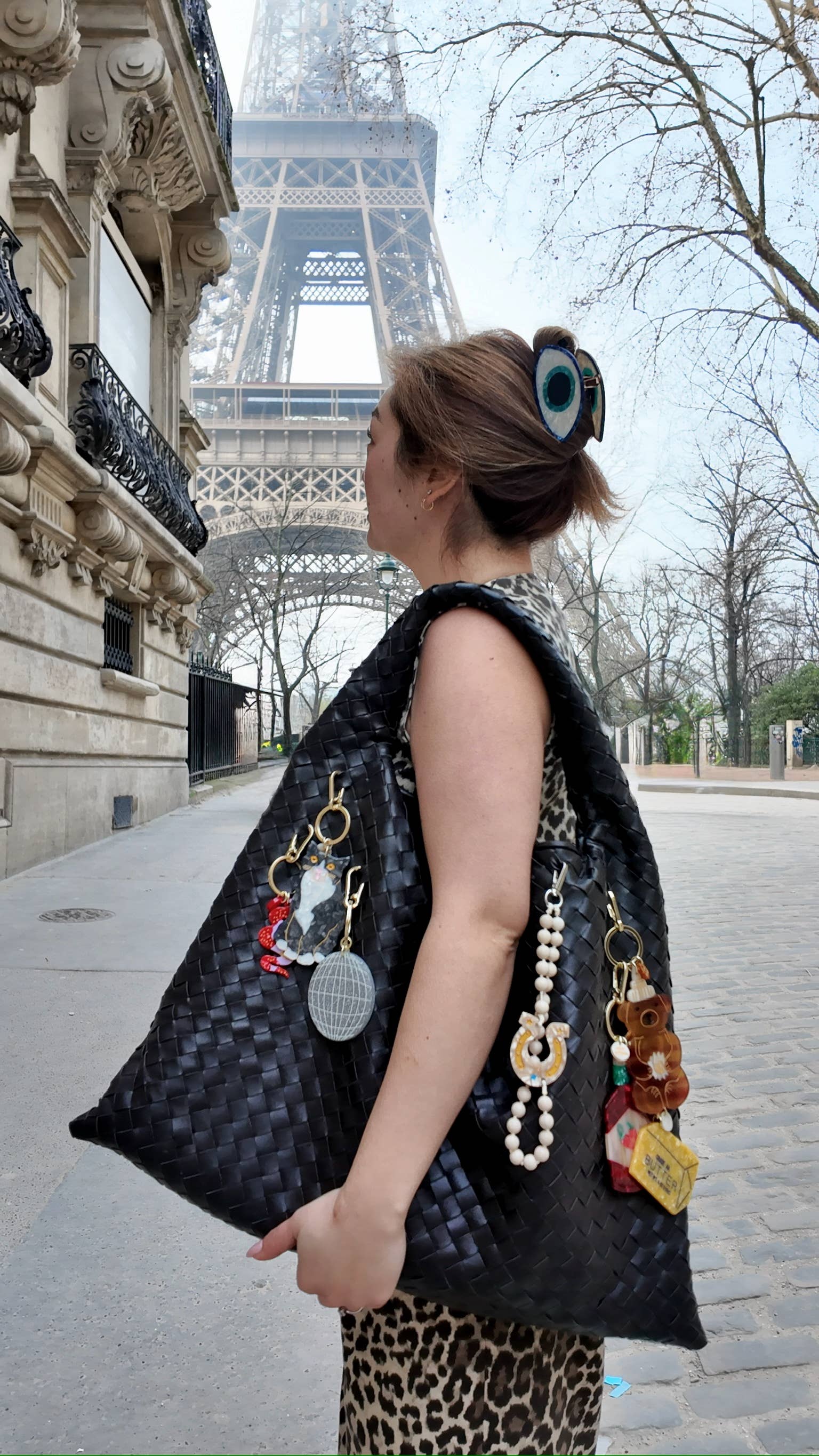 Woman holding a large black handbag with decorative elements in front of the Eiffel Tower.