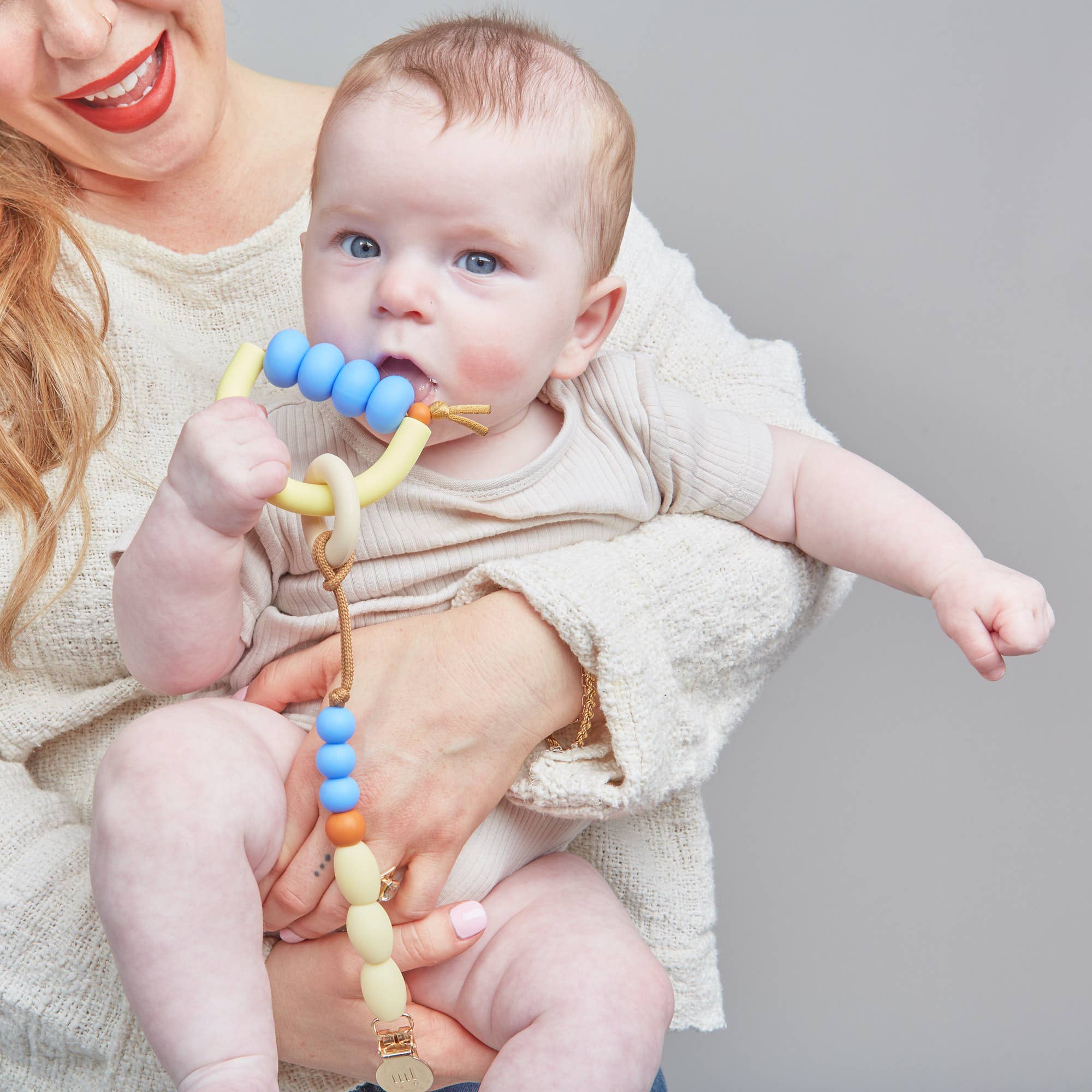 Baby holding a colorful teething toy with a neutral background