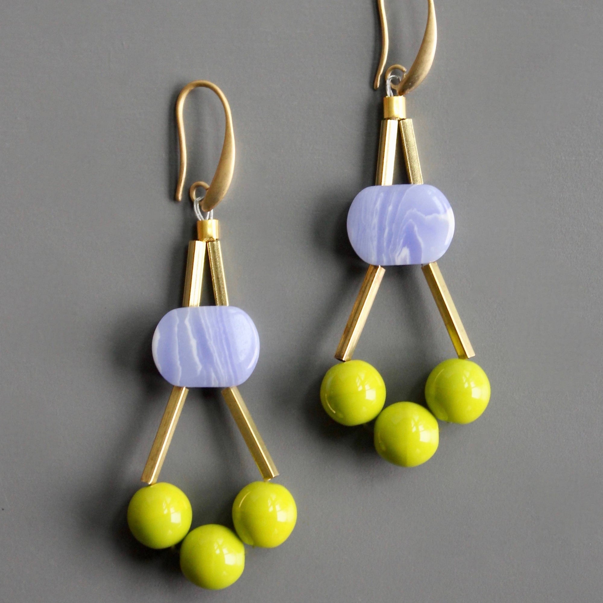 Gold earrings with purple and green beads on a gray background