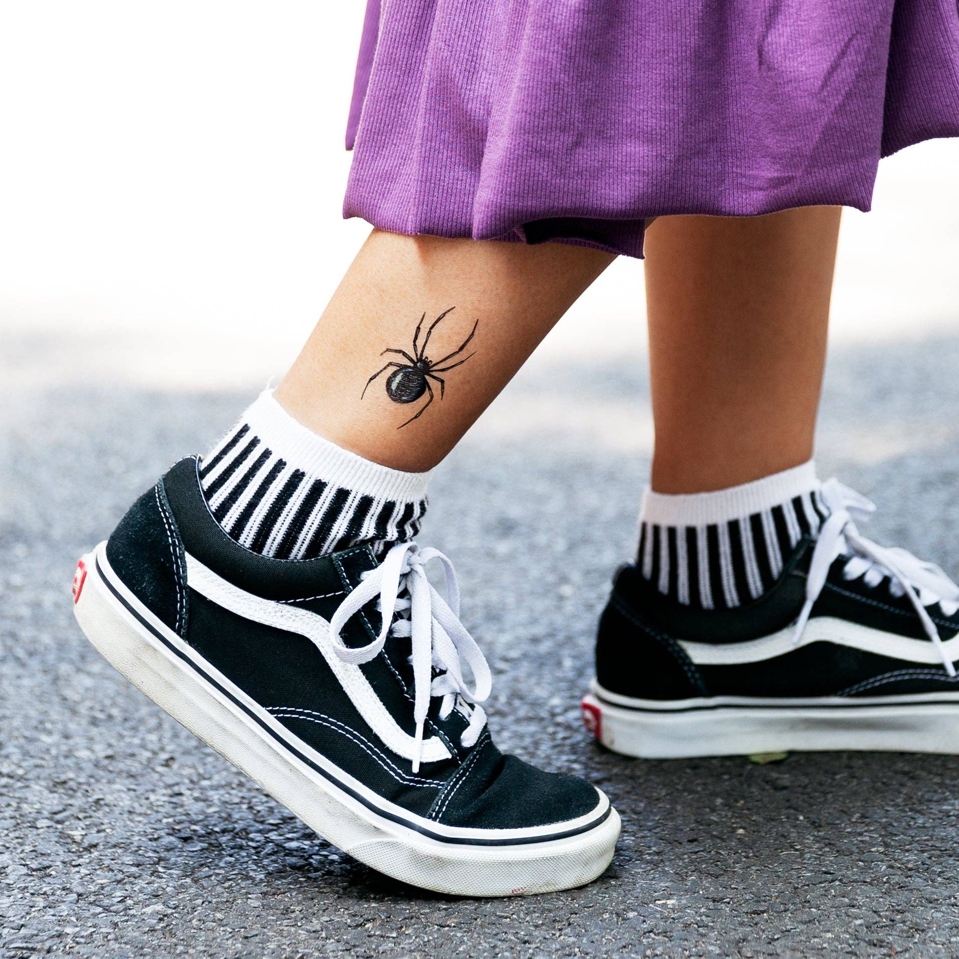 Person wearing black sneakers with white soles and a spider tattoo on the ankle.