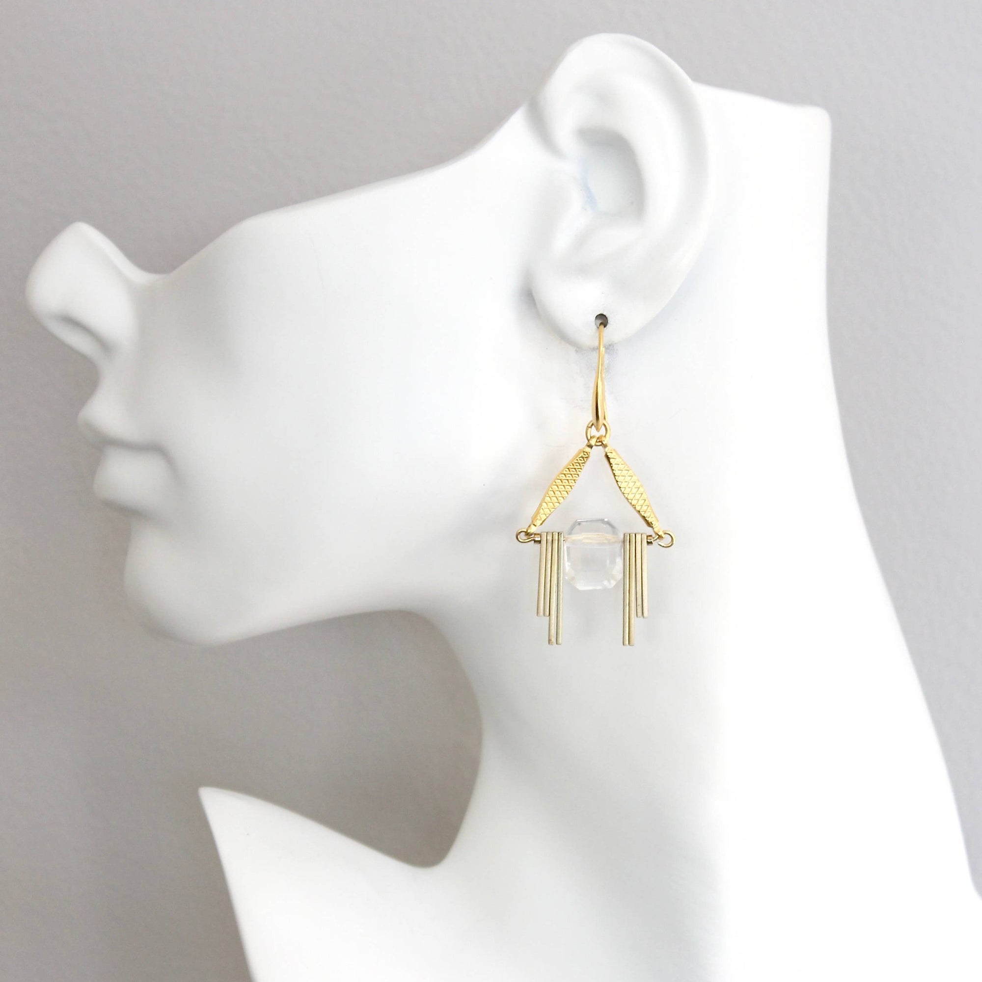 Gold geometric earrings on a white mannequin ear