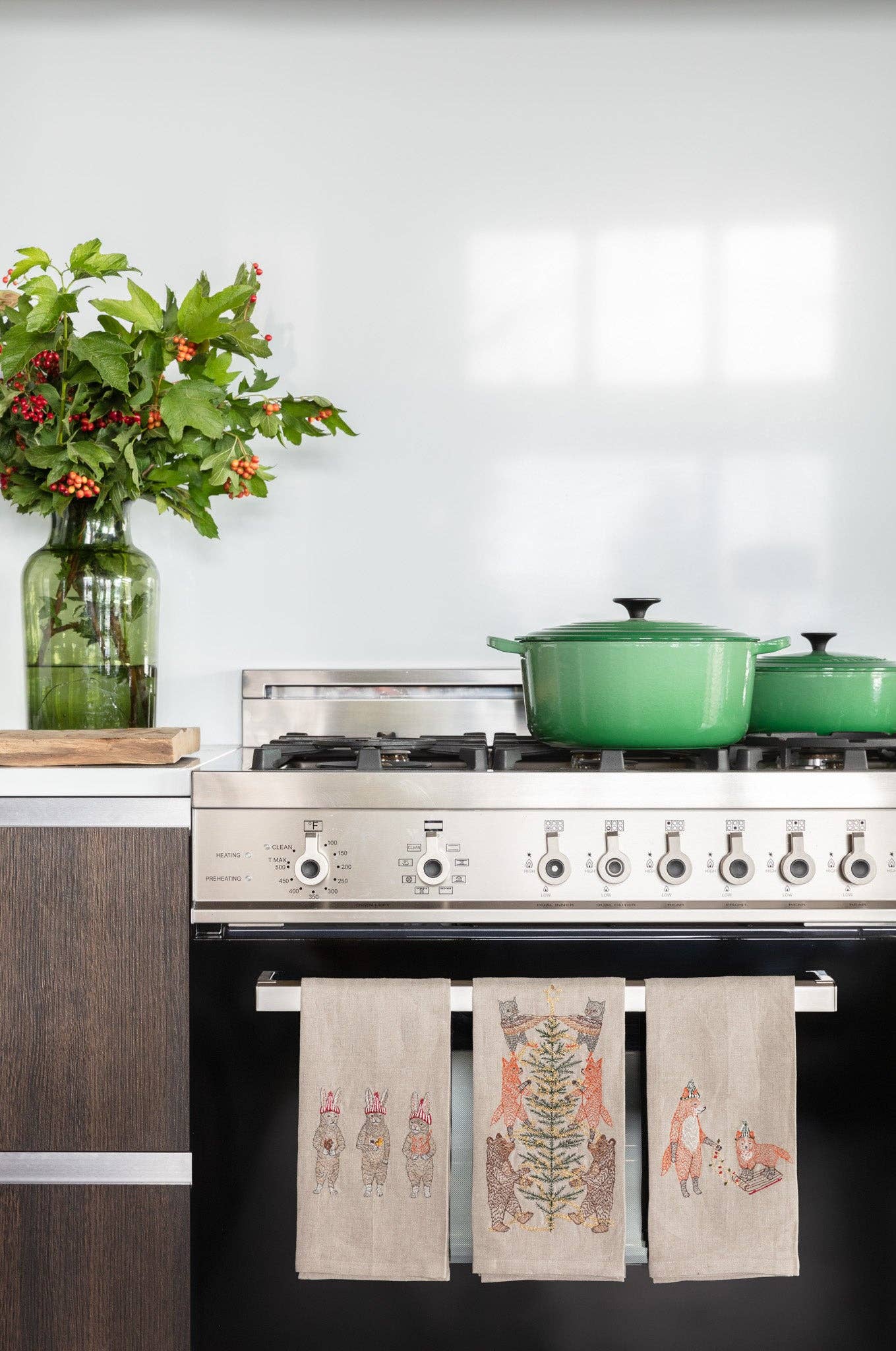 Kitchen with a stove, green pots, and decorative towels hanging on the handle.