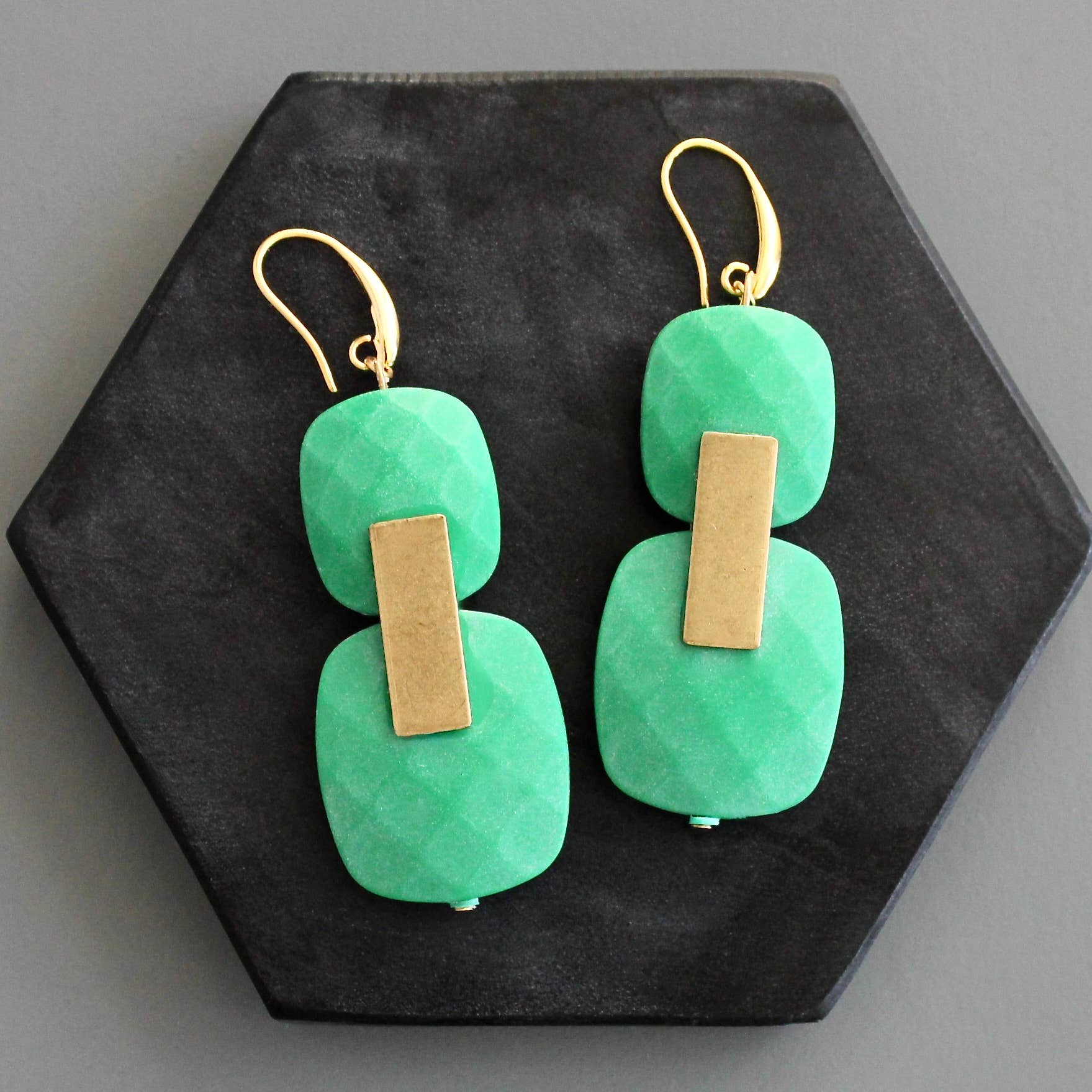 Green earrings with gold bars on a black hexagonal stand