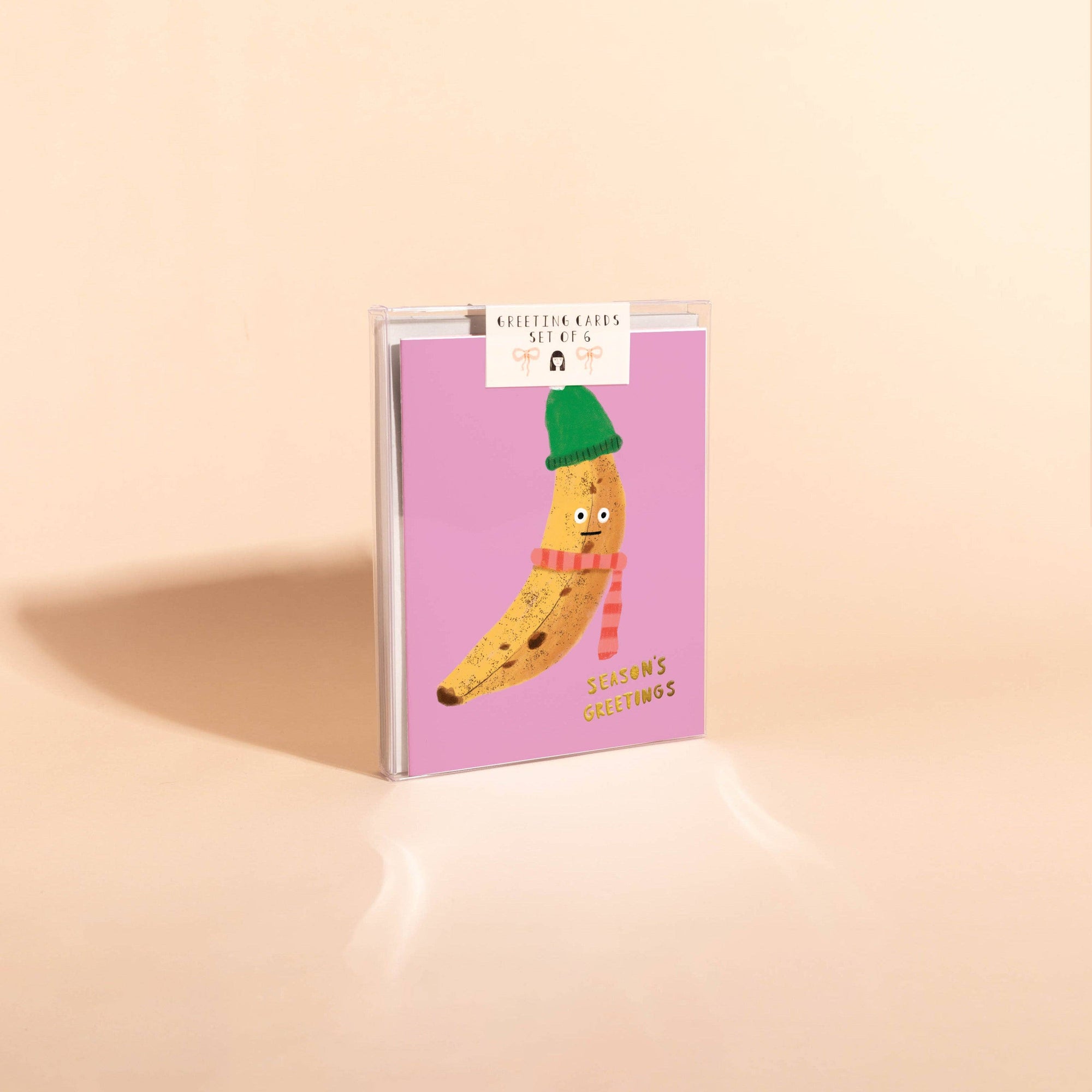 Notebook with a banana character wearing a green hat and pink scarf on a pink cover against a beige background