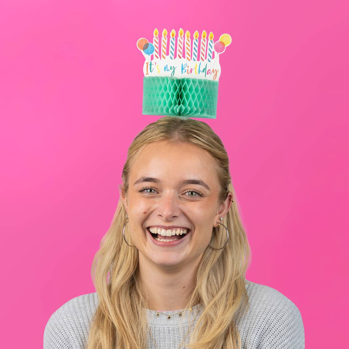 Woman with a birthday hat on her head against a pink background