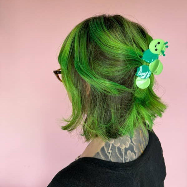 Person with green hair wearing a hair clip against a pink background