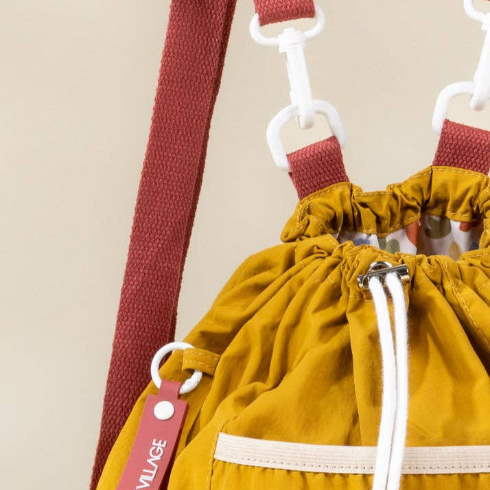 Yellow drawstring bag with a red strap and visible brand logo on a beige background