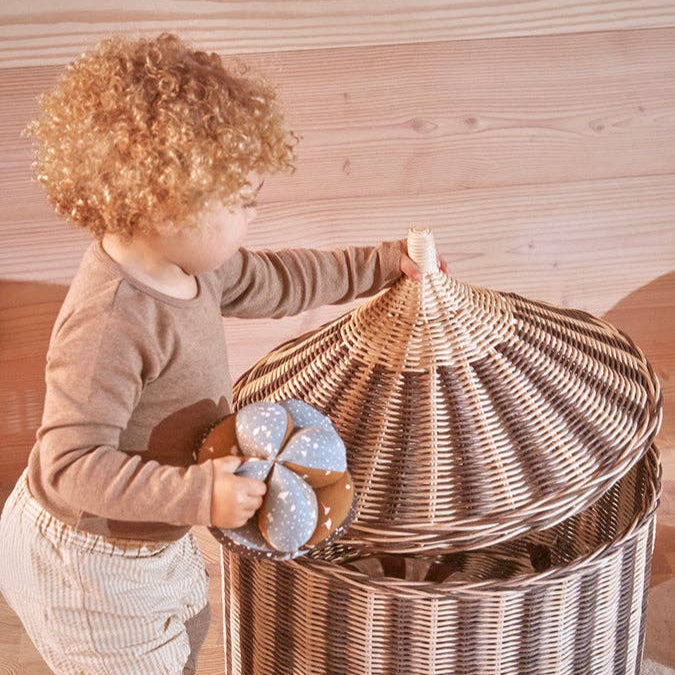 Child holding a large woven basket with a lid indoors.