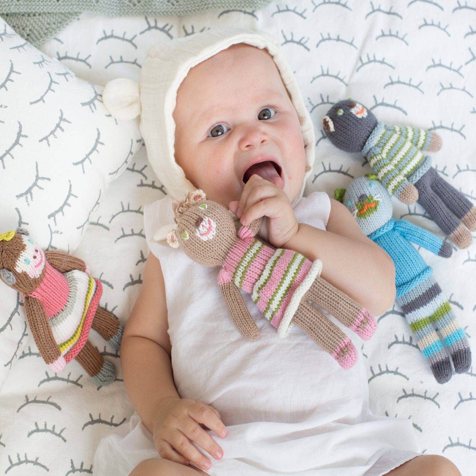 Baby lying on a patterned blanket with knitted toys