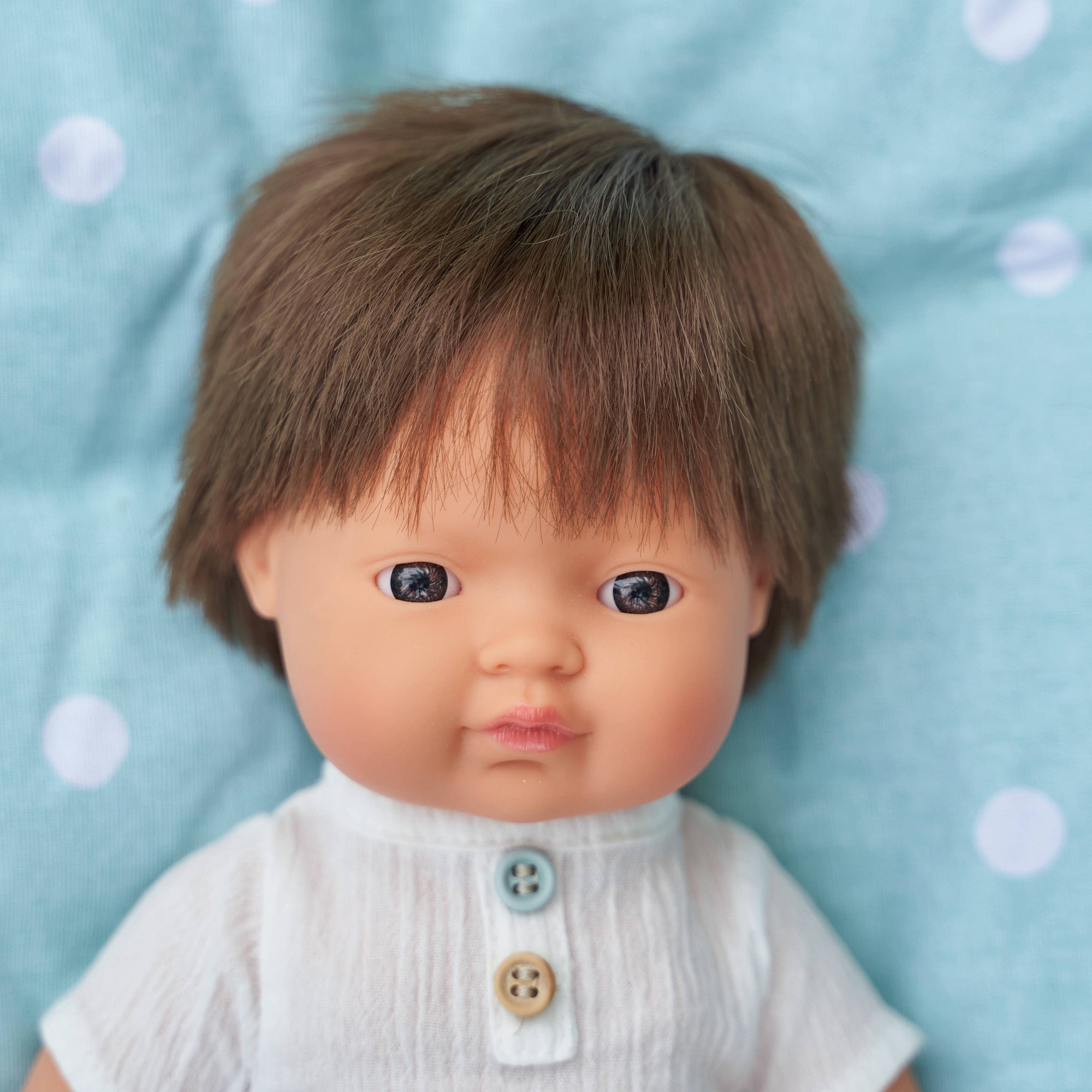 Child's doll with brown hair and a white outfit on a blue polka dot background