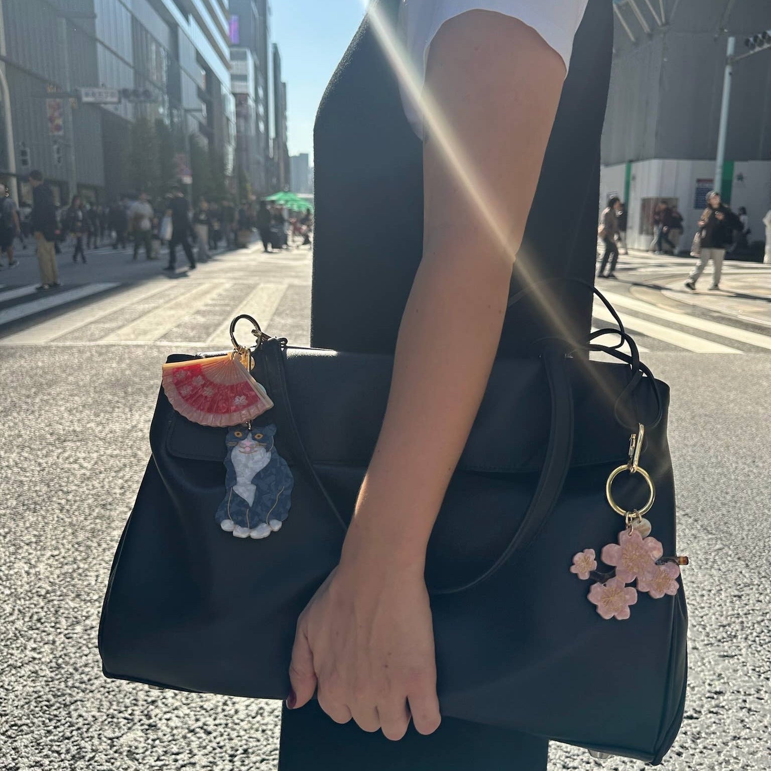Person holding a black handbag with decorative charms on a city street.