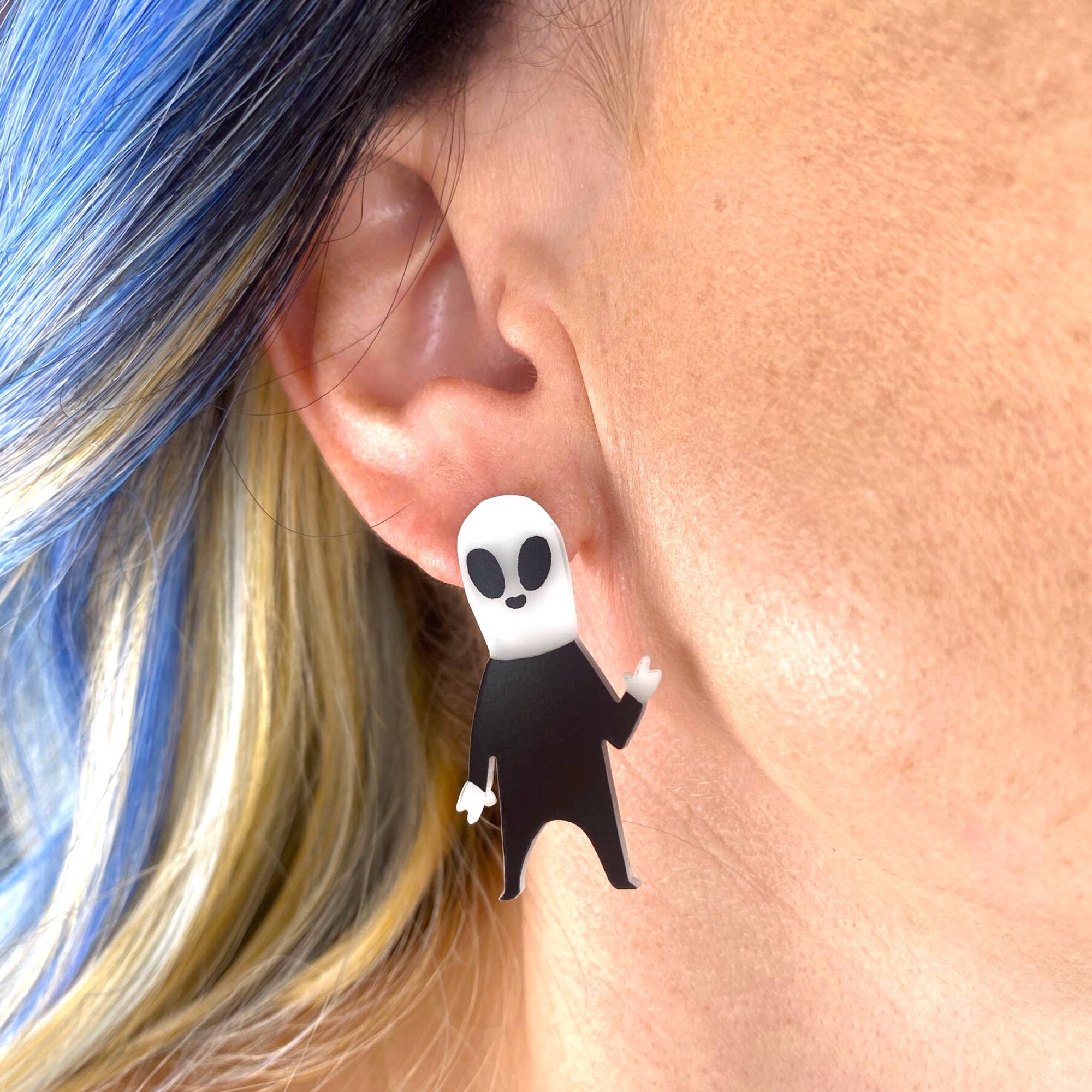 Ghost-shaped earrings worn by a person with blue and blonde hair.