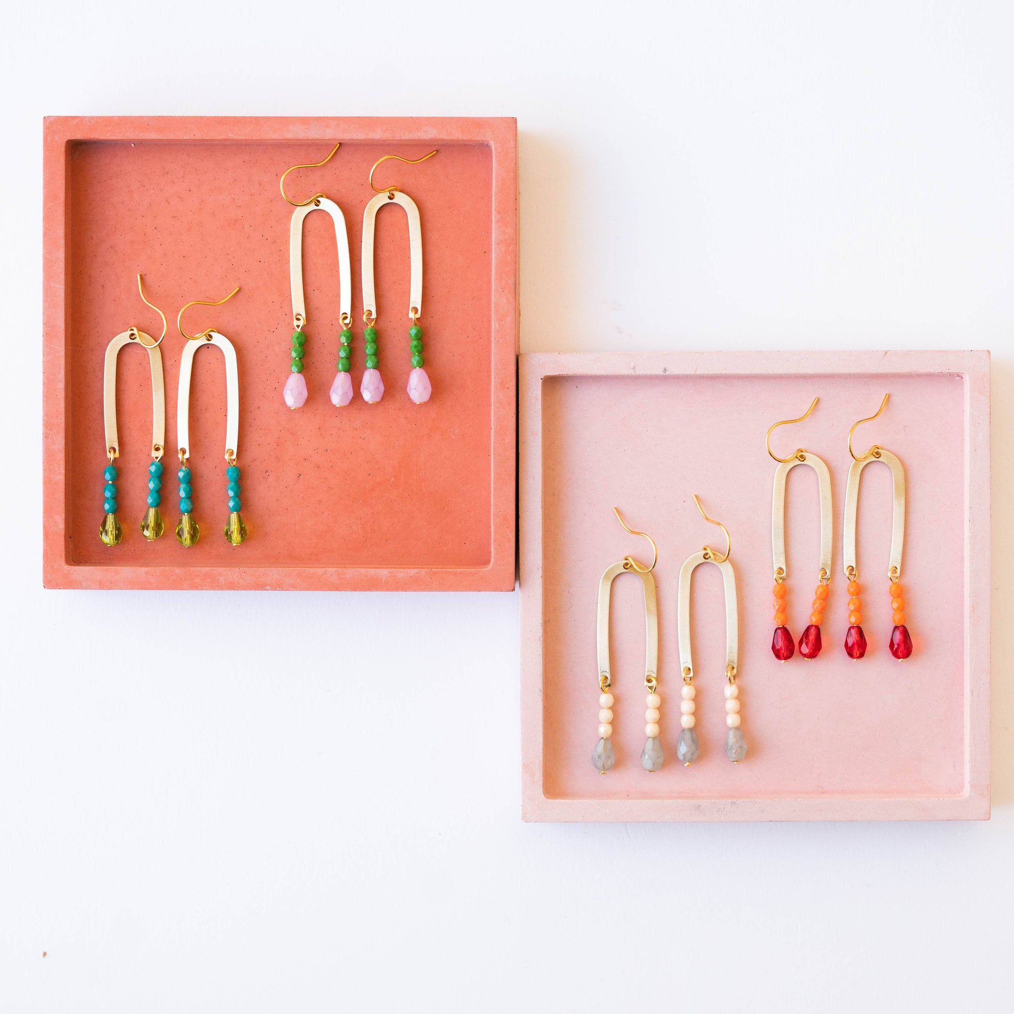 Colorful beaded earrings in pink and coral display boxes on a white background