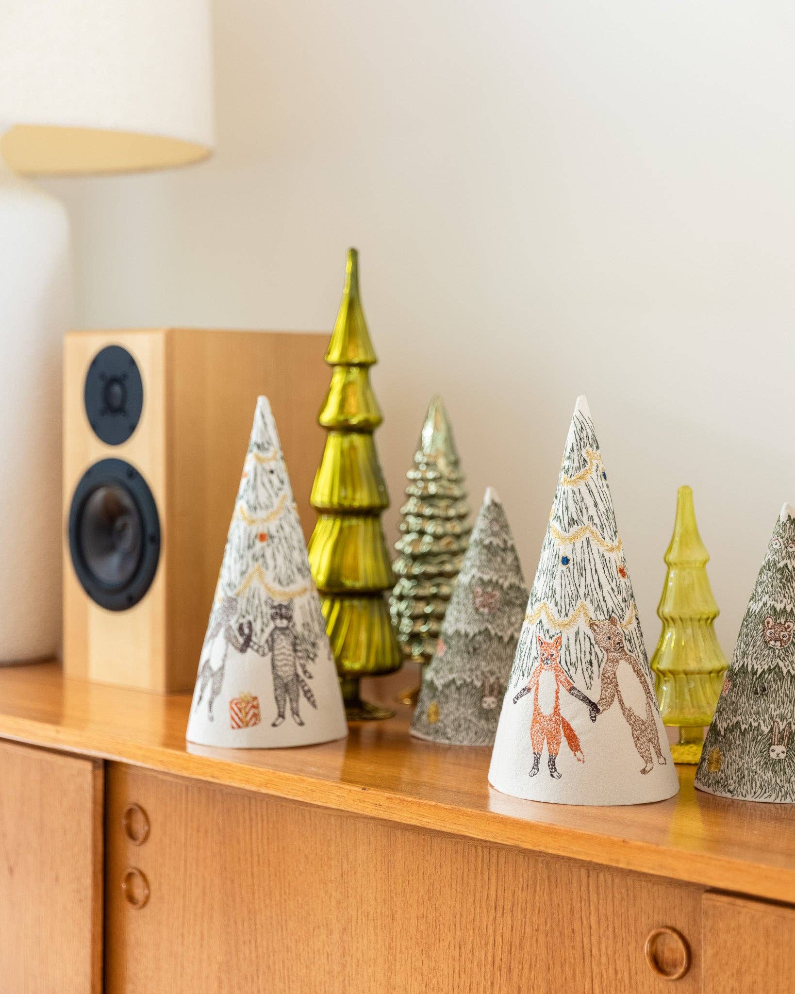 Decorative Christmas trees on a wooden surface with a speaker in the background
