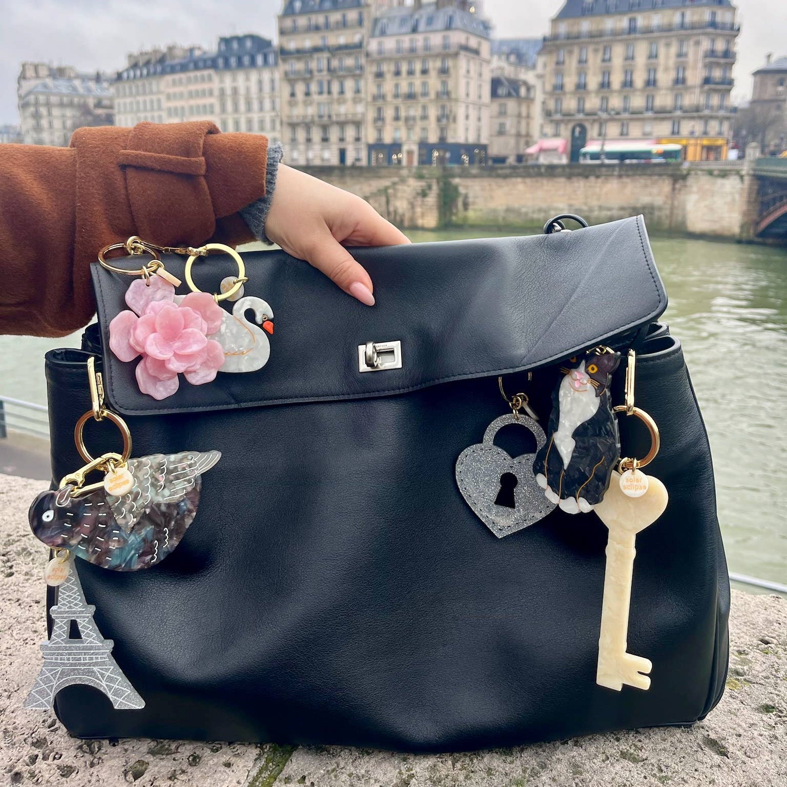 Black backpack with decorative charms held by a person in an urban setting.