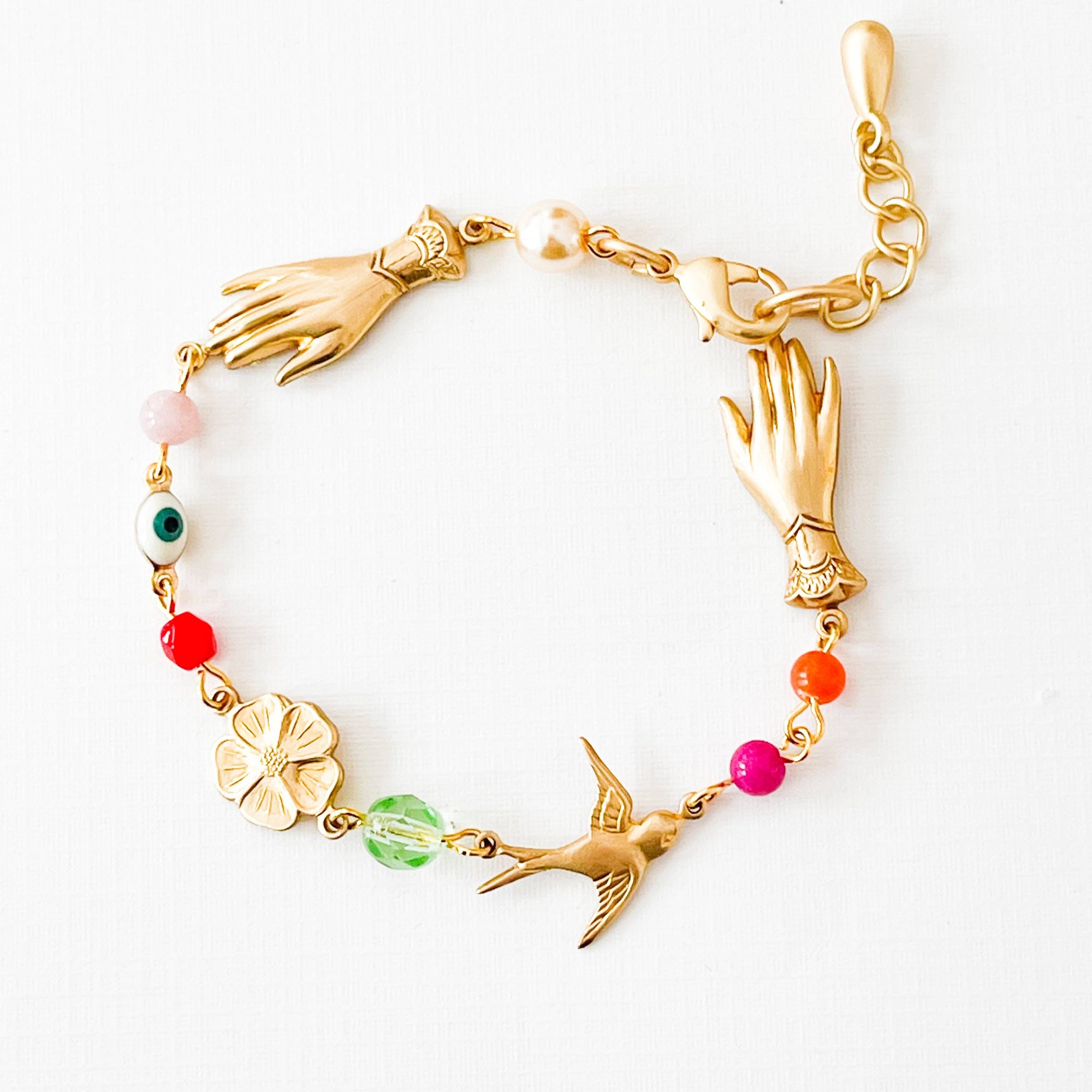 Gold bracelet with hand, bird, and floral charms on a white background
