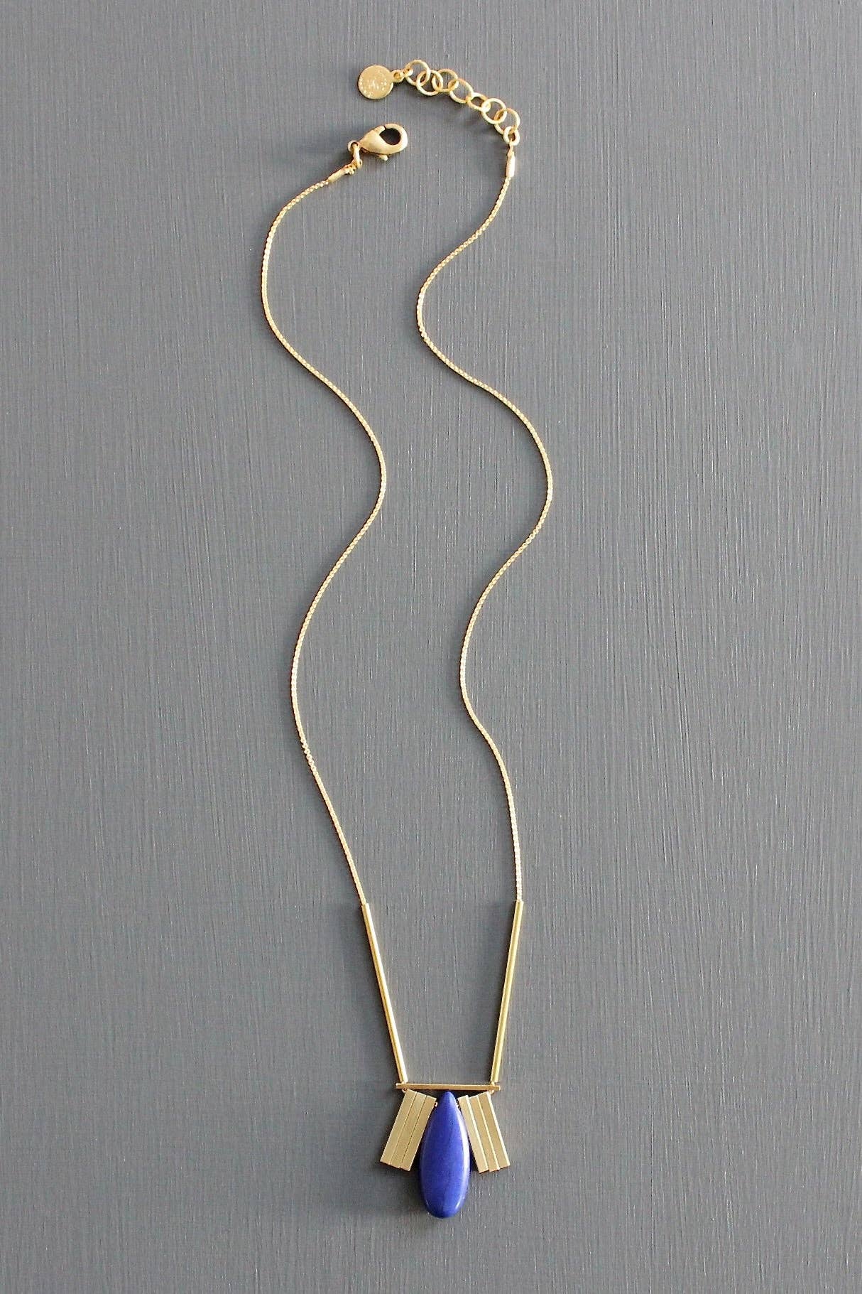 Gold necklace with a blue pendant on a gray background
