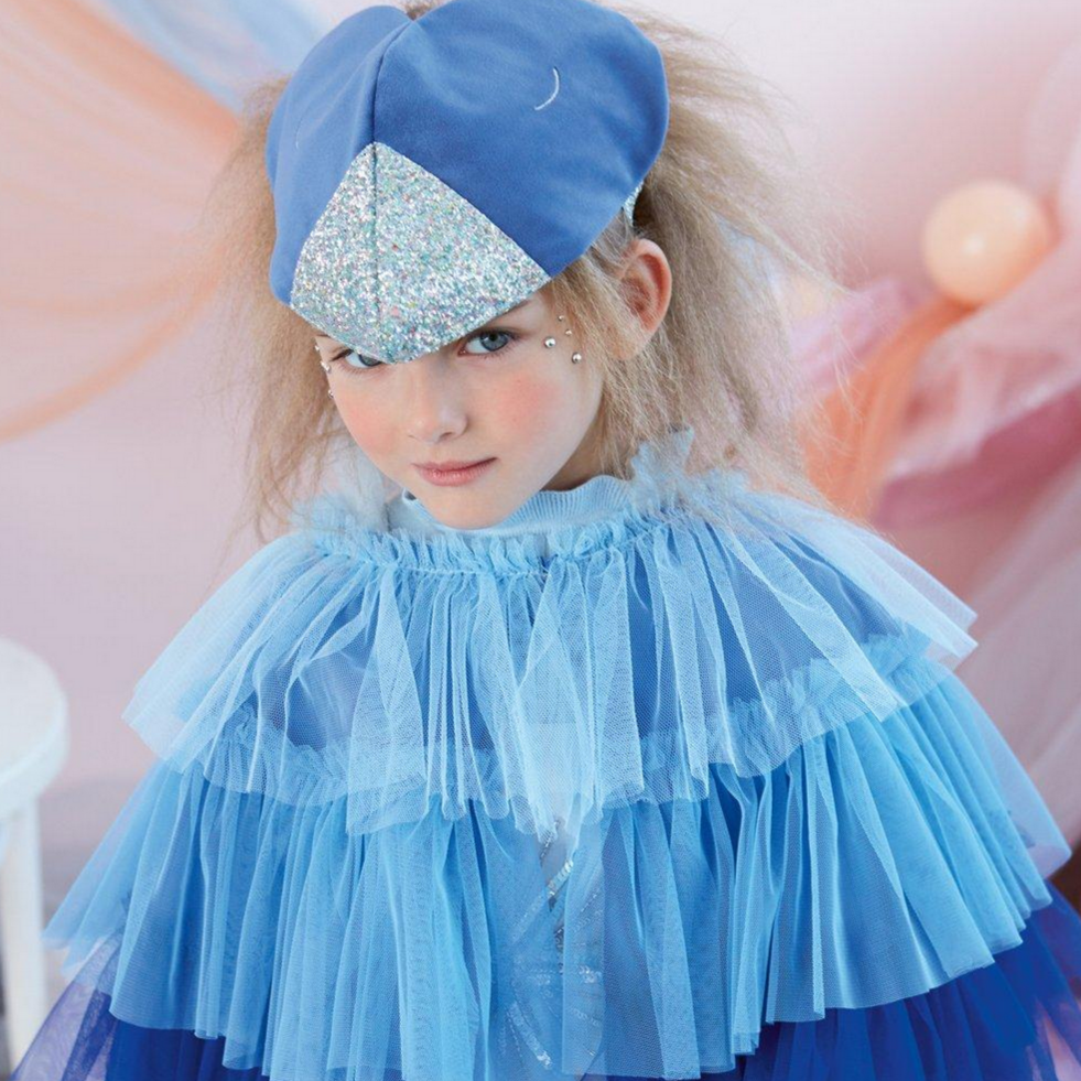 A child wearing a blue bird costume with wings and a tail made of ruffled tulle, and a blue velvet headdress with embroidered silver eyes and a glittery beak.