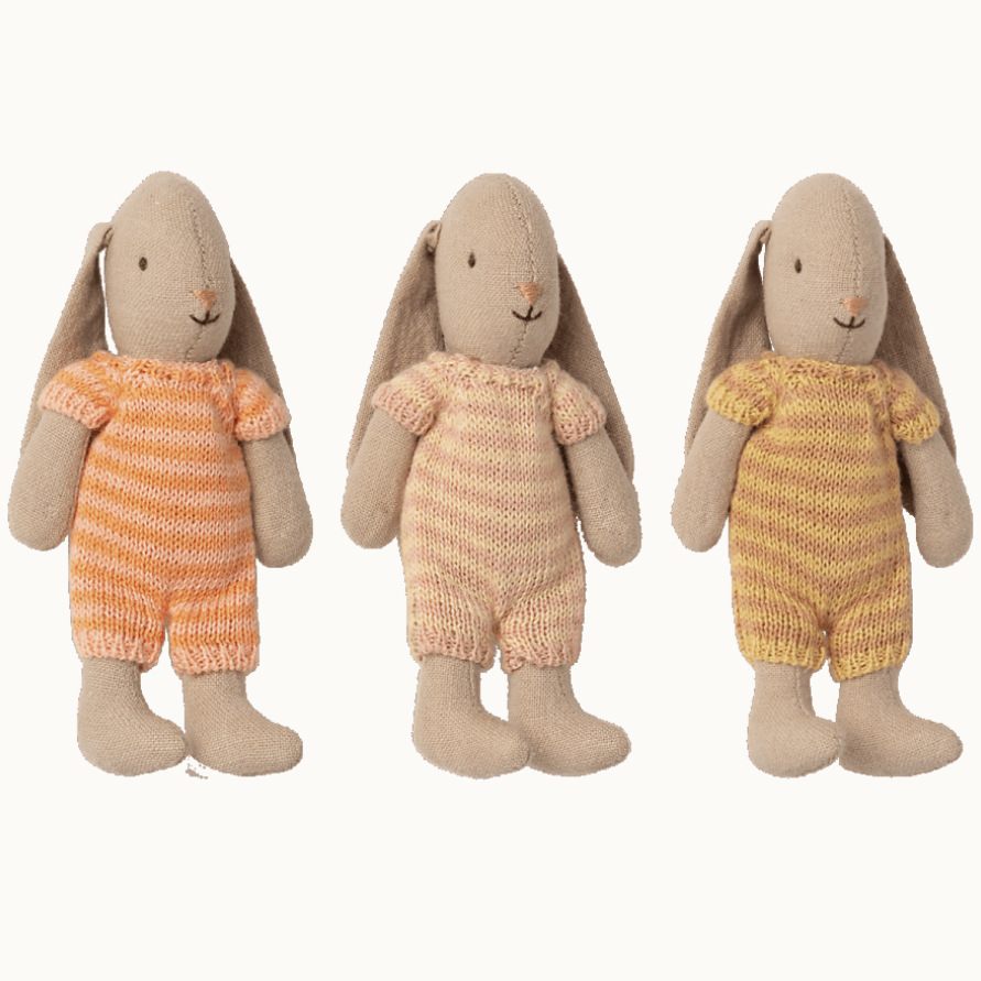 Three toy rabbits, each wearing a striped knitted suit in different color combinations (orange and beige, beige and brown, yellow and brown), standing side by side.