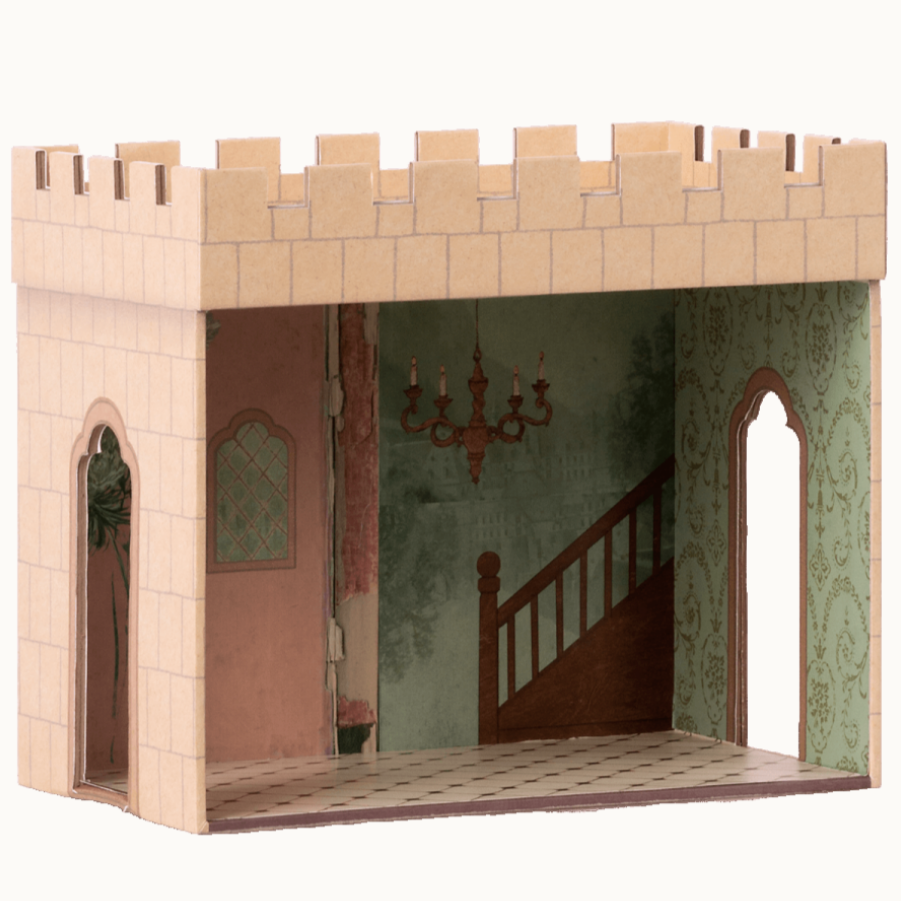 A toy castle hall with a beige exterior and a staircase leading to a landing with a chandelier. The interior features a room with pink walls and a green patterned wallpaper.