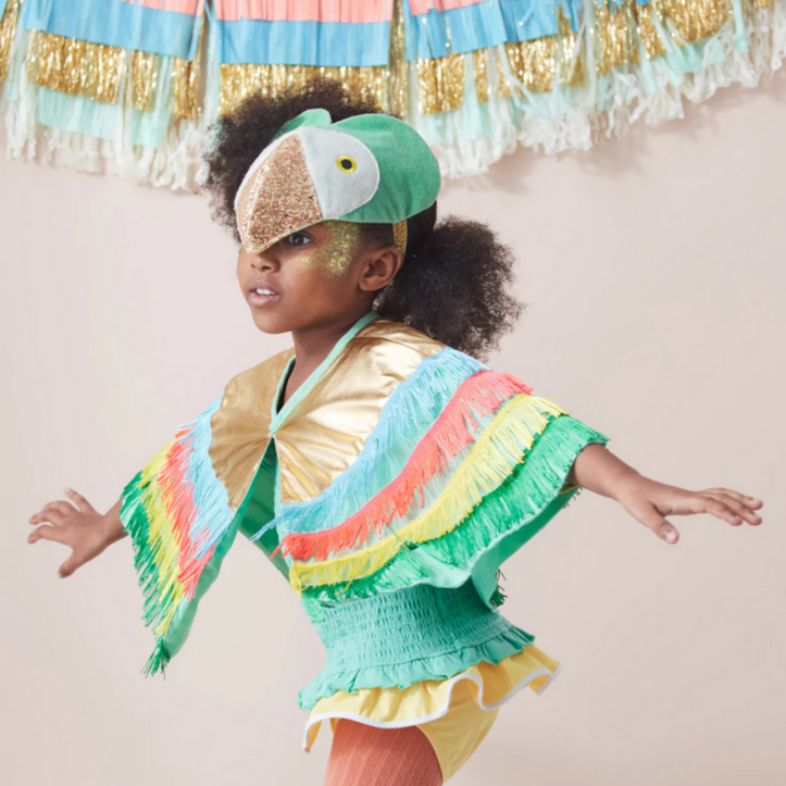 A child wearing a colorful parrot costume with a winged cape and a green velvet headdress with glitter details.