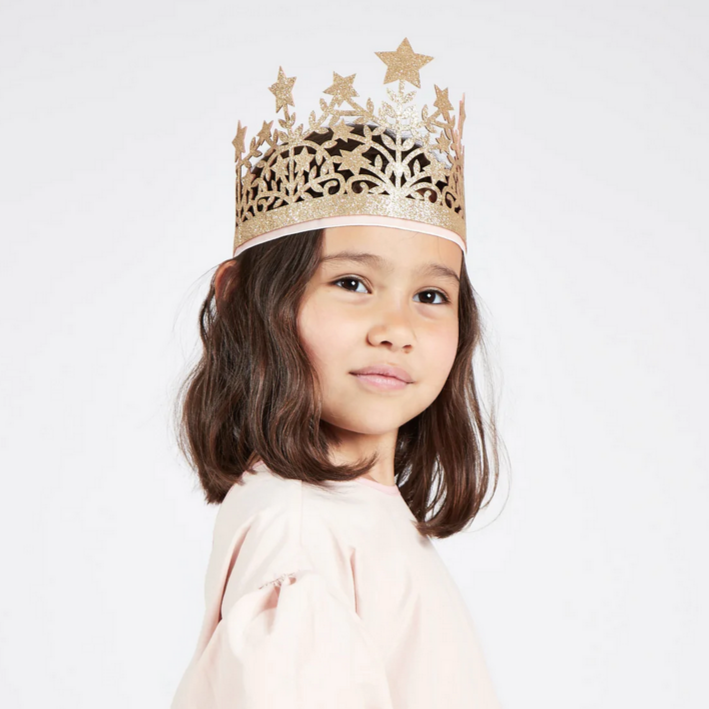A child wearing a gold glitter fabric crown with a large star centerpiece and a dusty pink velvet band.