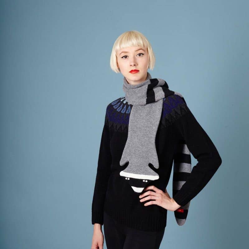 Person wearing a black sweater with a large gray and black patterned scarf against a blue background