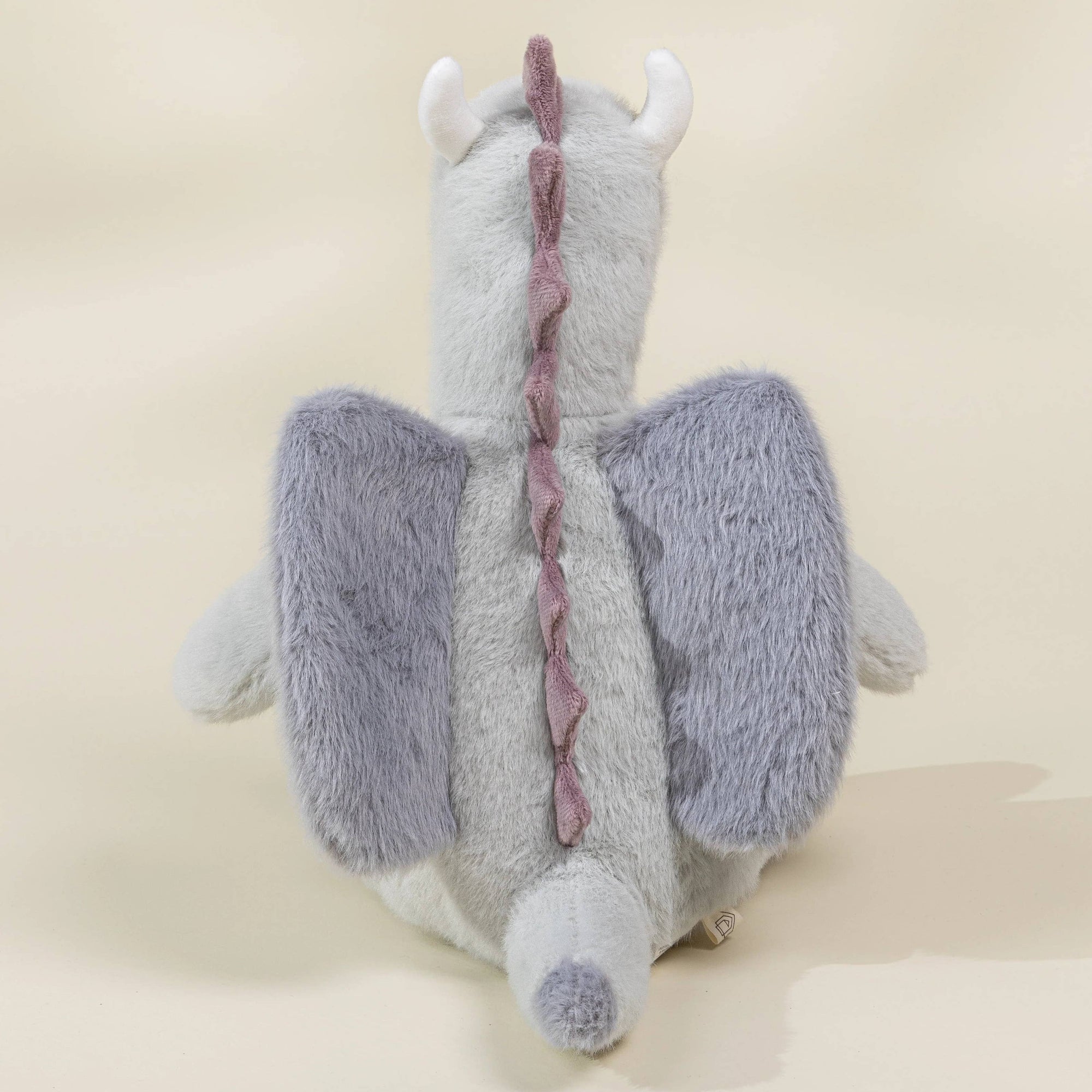 Gray plush dragon toy with purple wings on a beige background