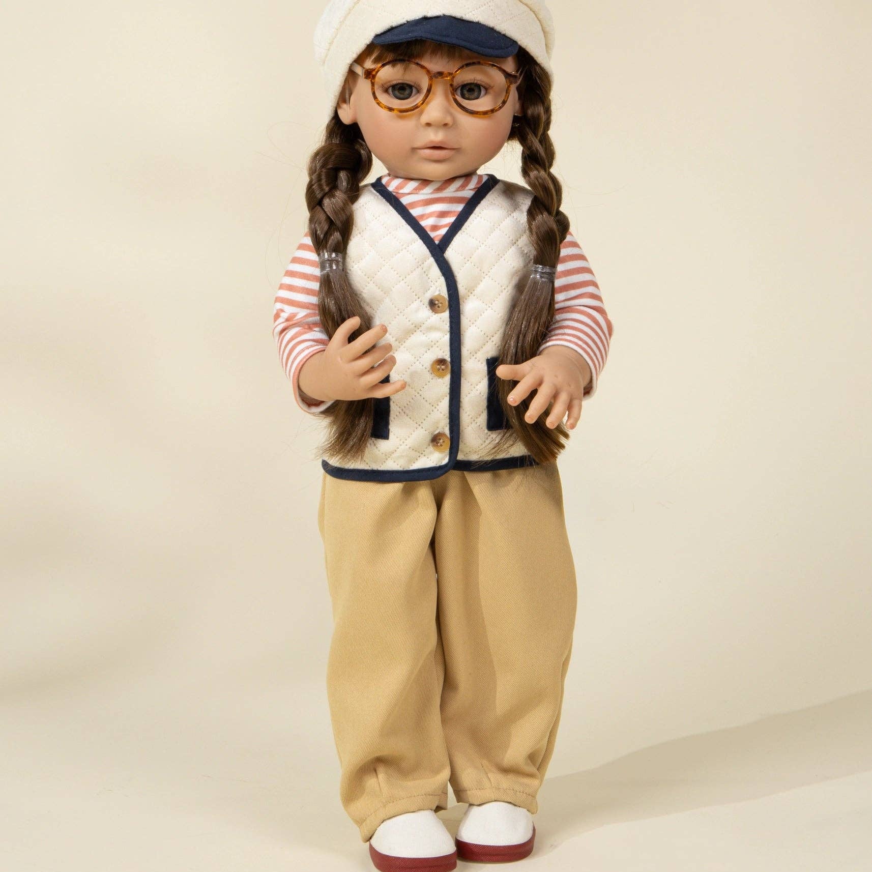 Doll wearing a vintage outfit with a vest, pants, and hat on a beige background
