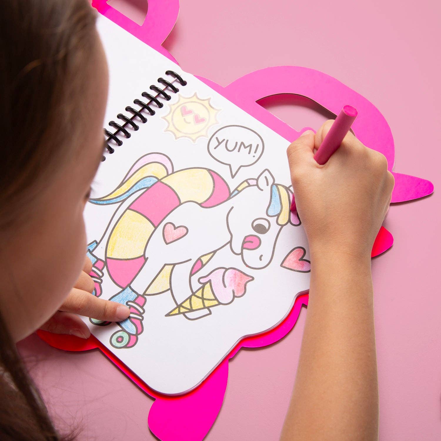 Child coloring a unicorn with ice cream on a pink table