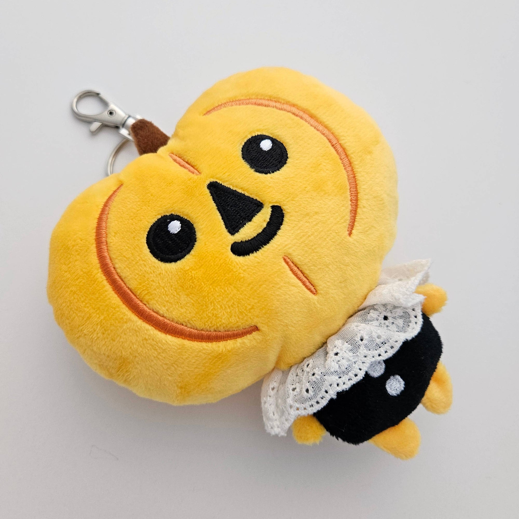 Plush keychain with an orange face and black and white outfit on a light gray background