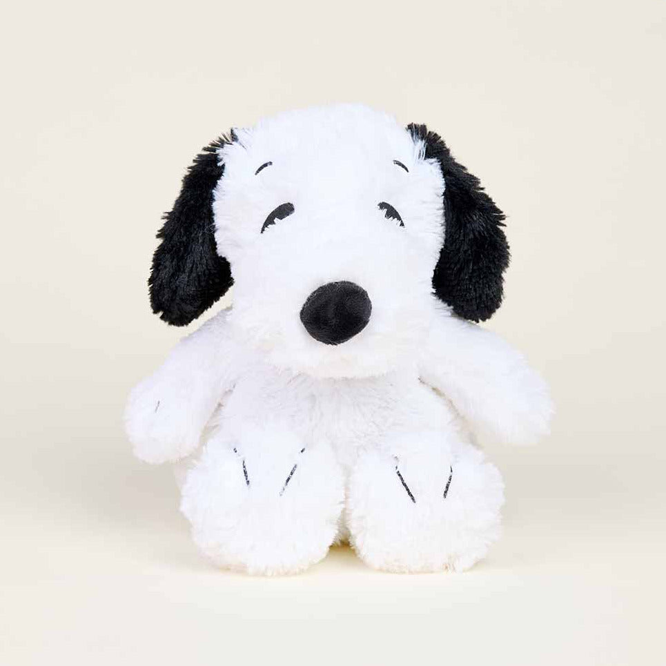 A plush toy dog in a white and black color scheme, styled like Snoopy, sitting against a solid light beige background.
