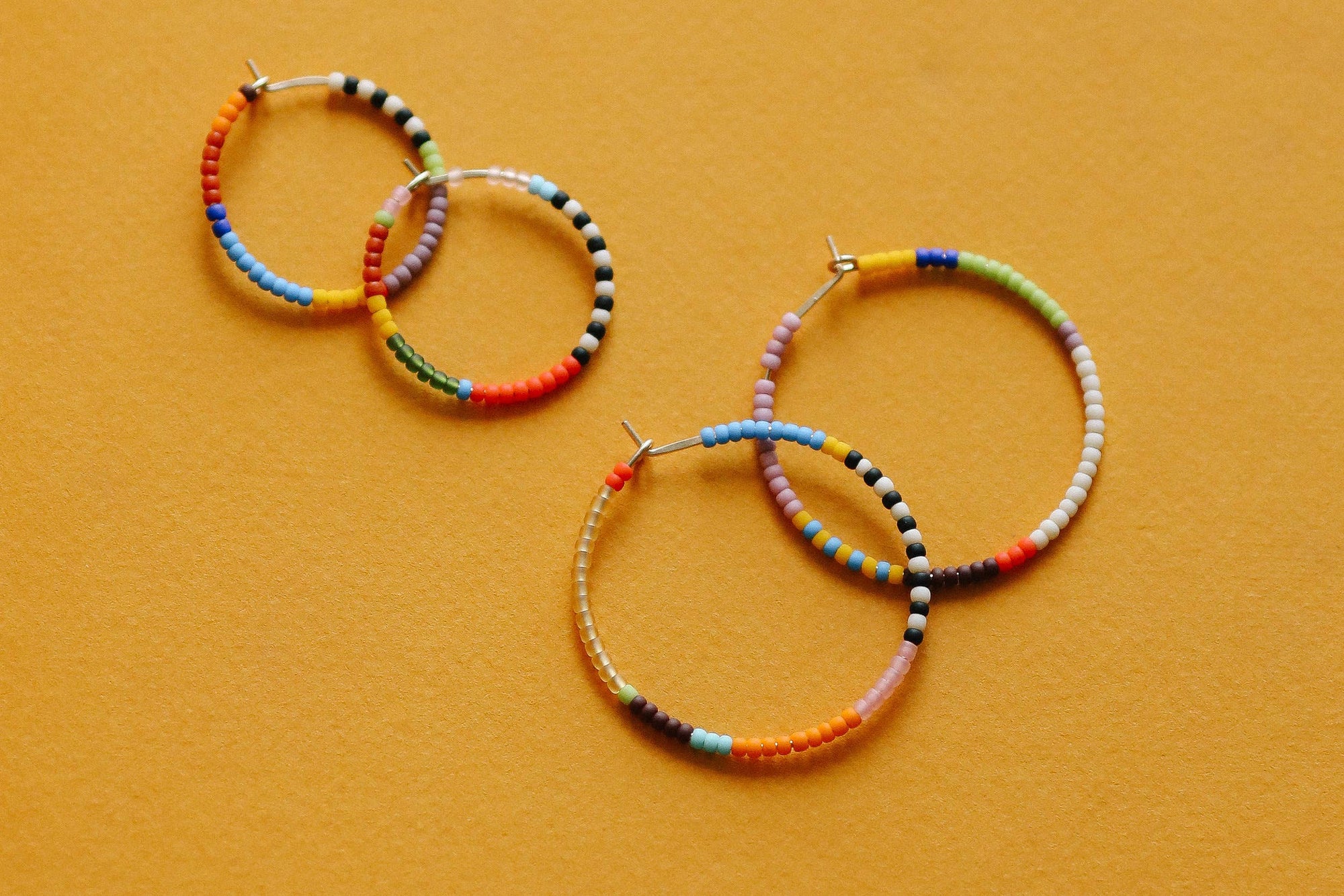Set of colorful beaded hoop earrings on a mustard yellow background