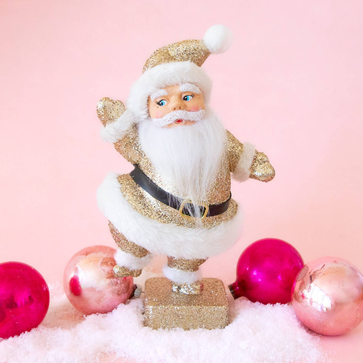 Decorative Santa Claus figure with gold glittery outfit on a pink background with pink and red ornaments.