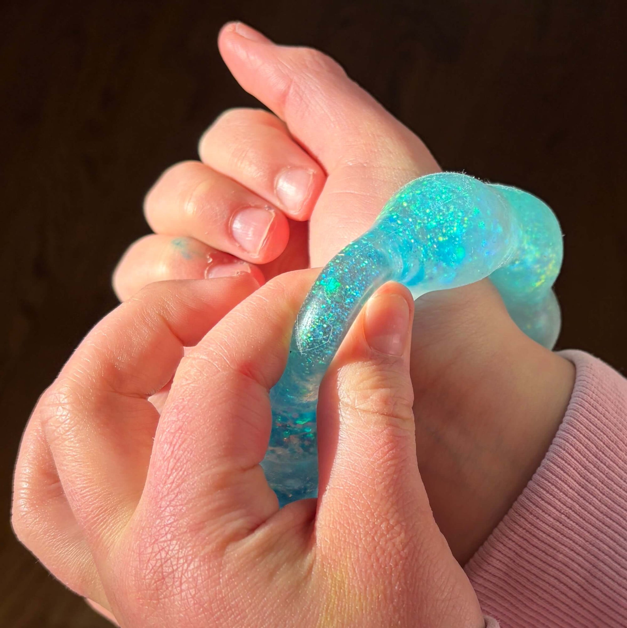 Close-up of hands holding a blue gel-like object against a wooden background