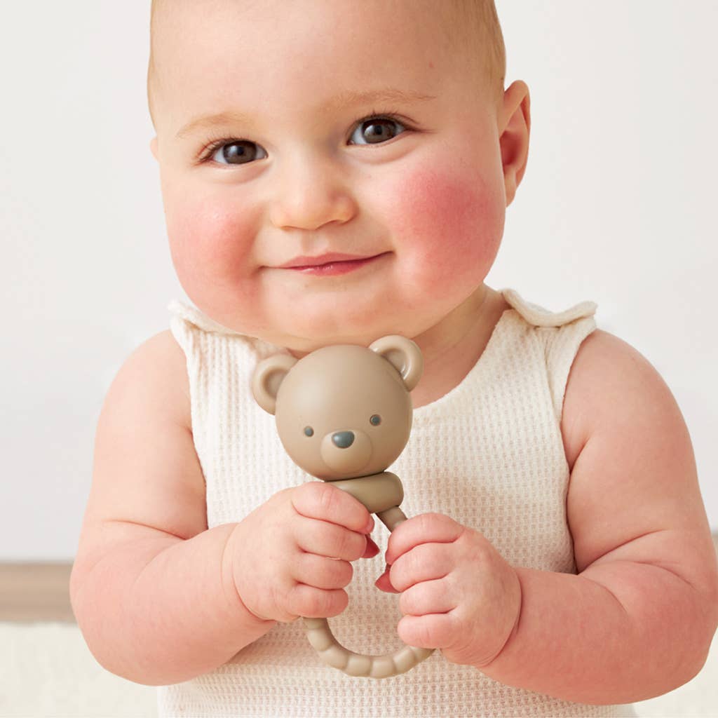 Baby holding a teddy bear-shaped teething ring against a plain background