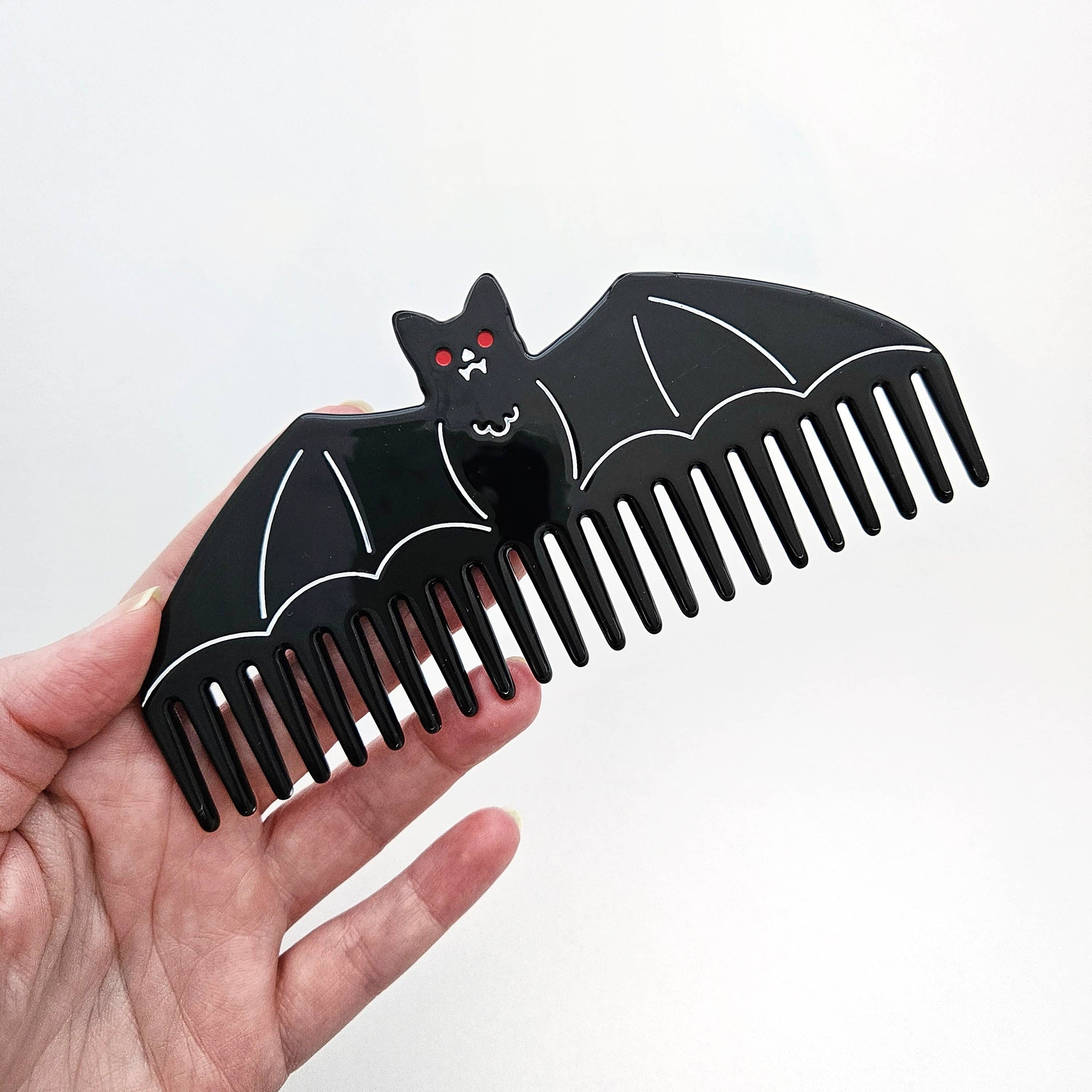 Black bat-shaped comb held in a hand against a white background