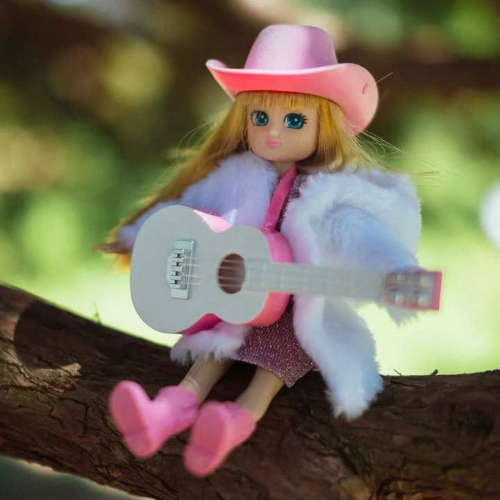 Doll with pink cowboy hat and guitar sitting on a tree branch