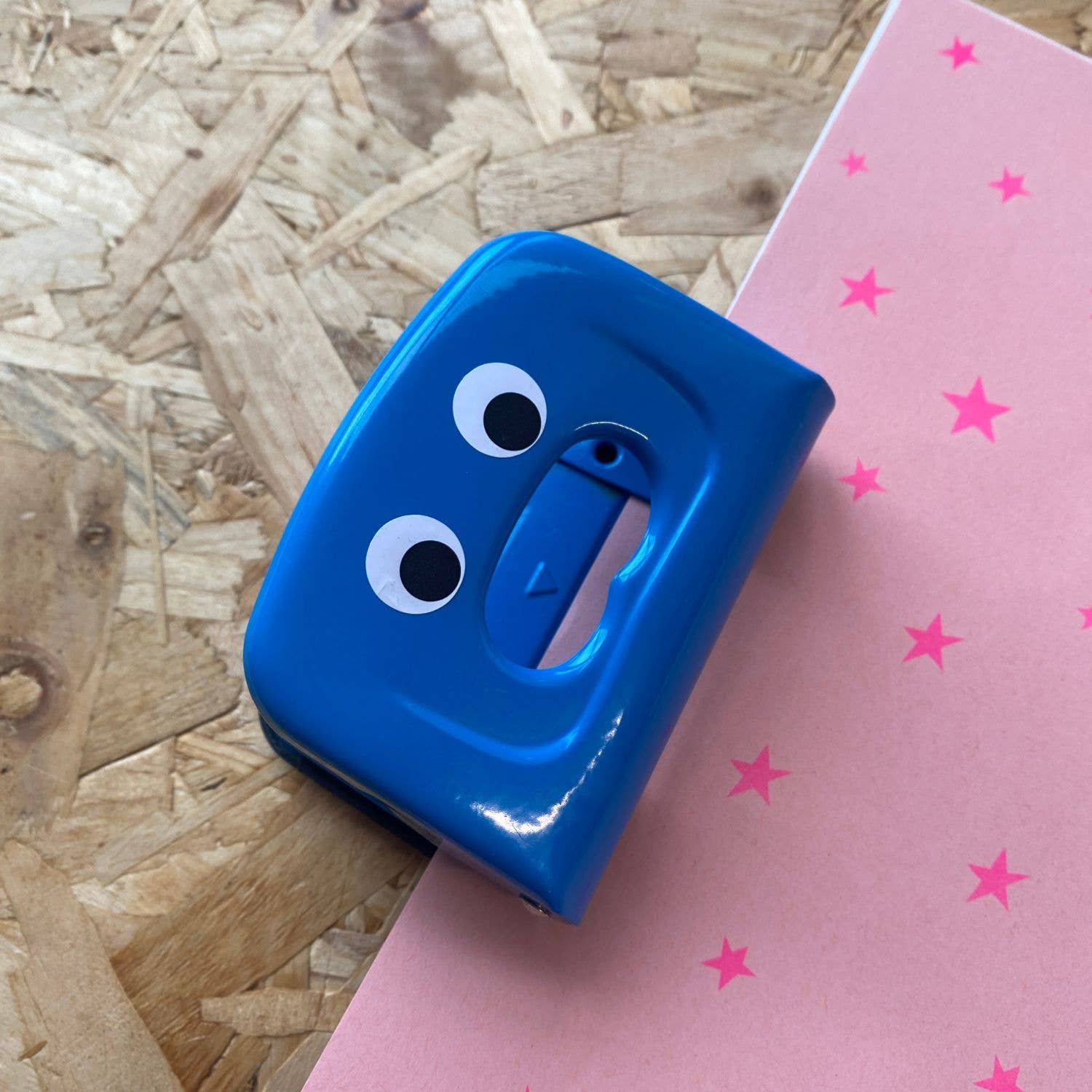 Blue paper punch with googly eyes on a pink surface with star patterns