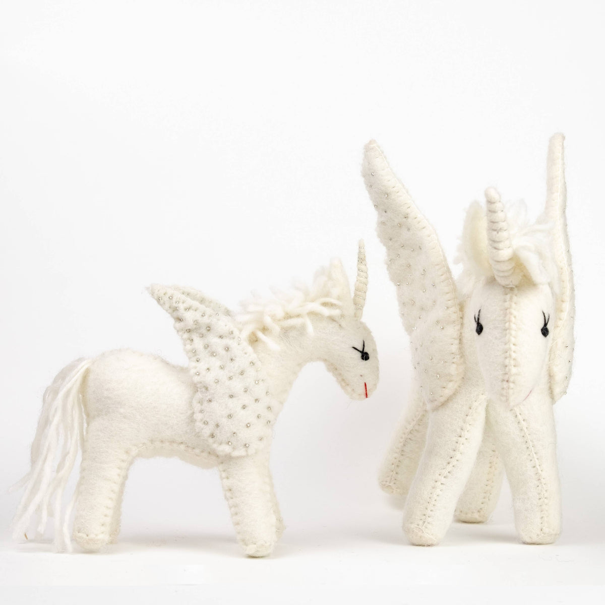 Two white knit unicorn toys on a light gray background