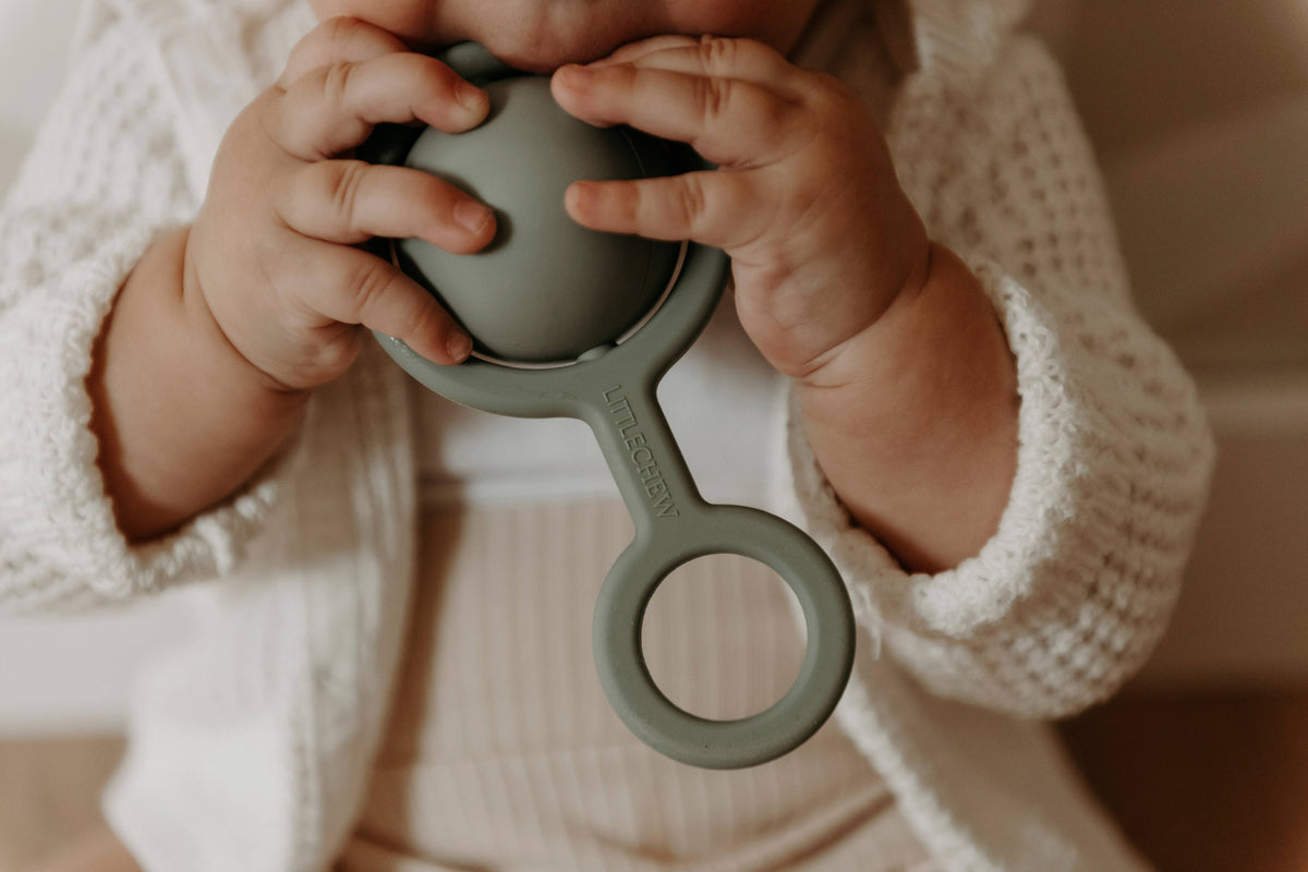 Child's hands holding a green teething ring with a blurred background