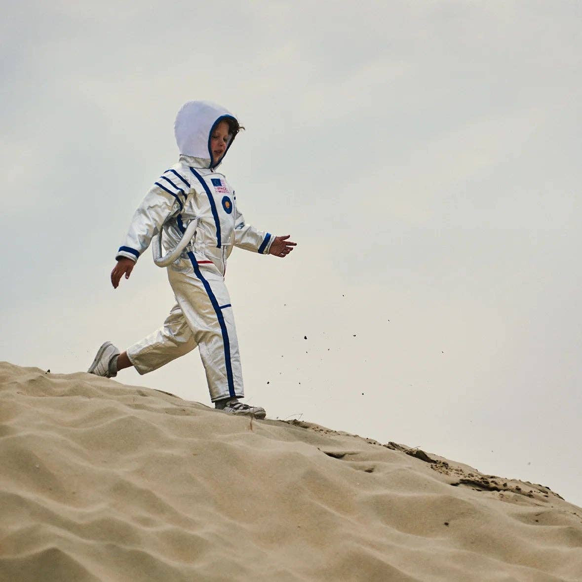 Person in an astronaut suit walking on sand with a clear sky