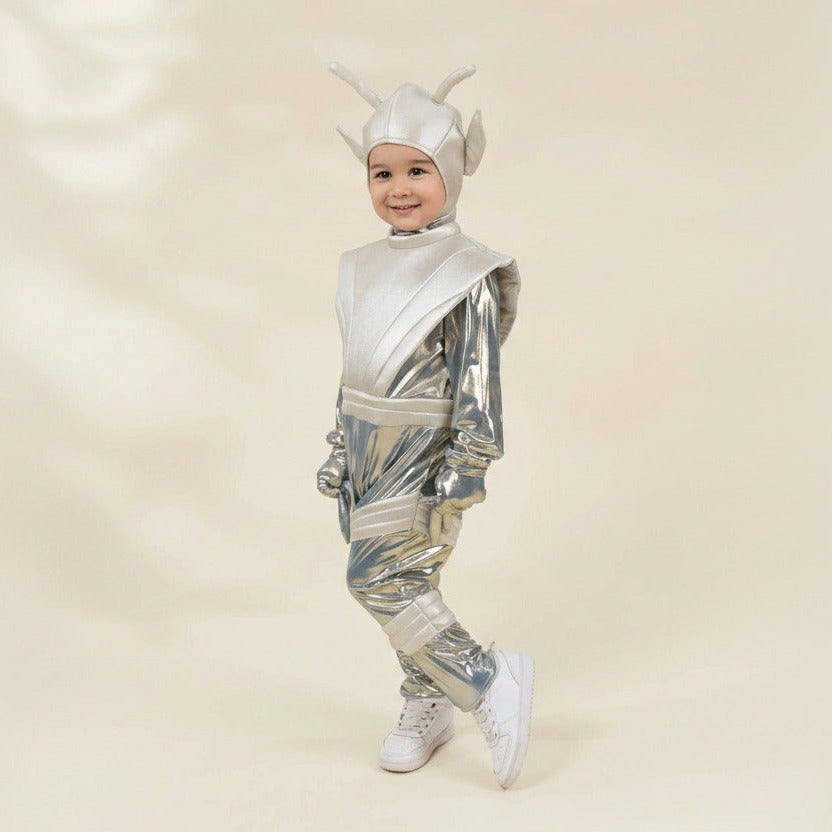 A young child modeling a shiny silver futuristic alien or robot costume with a matching helmet, standing against a plain beige studio background.