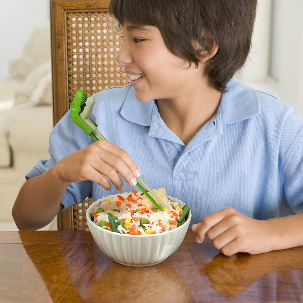 Child eating a bowl of salad with a smile at a dining table.