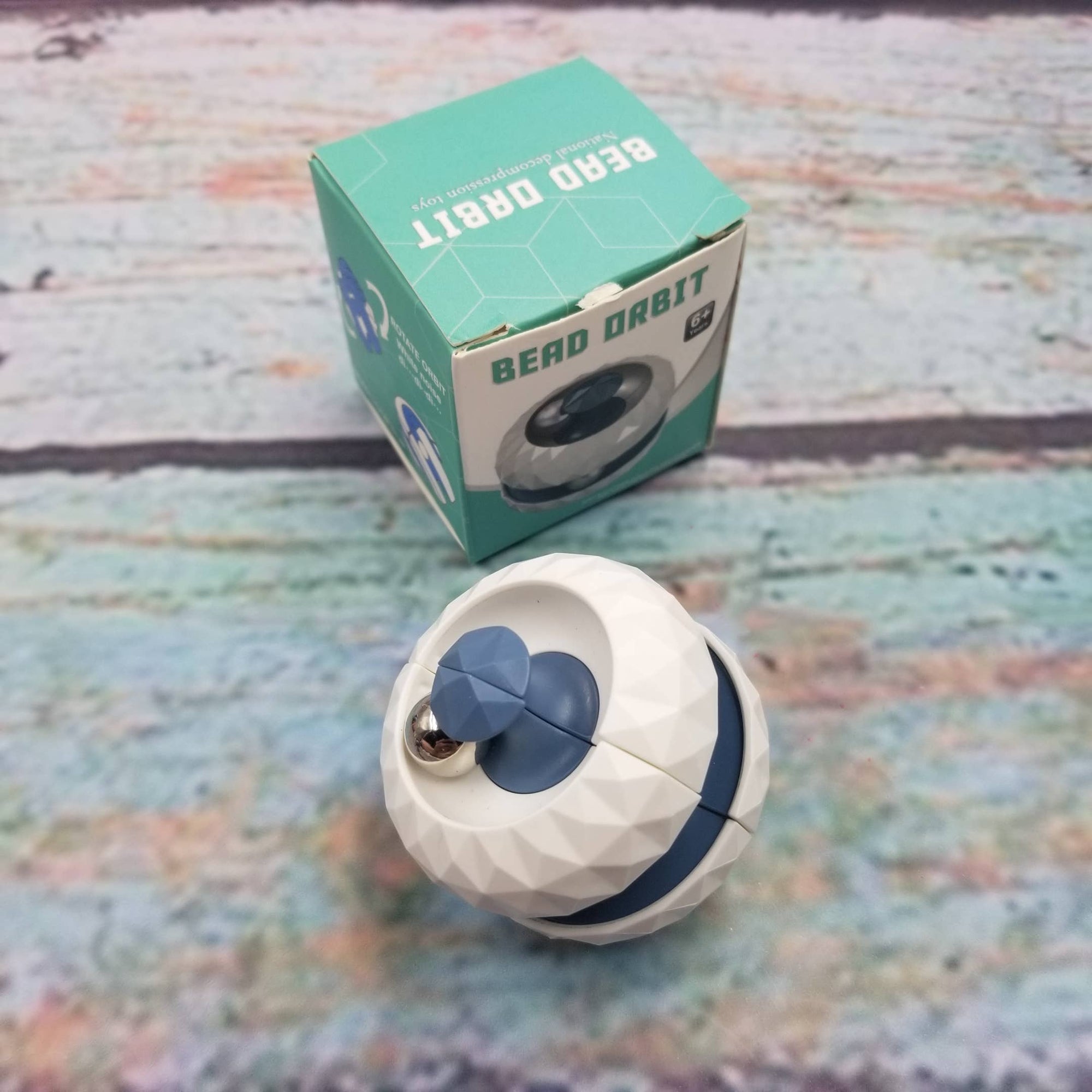 White and blue pet toy with 'Bead Orbit' packaging on a textured surface