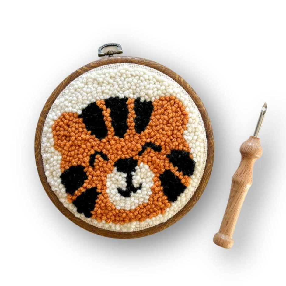 Embroidery hoop with a tiger design and a wooden crochet hook on a white background