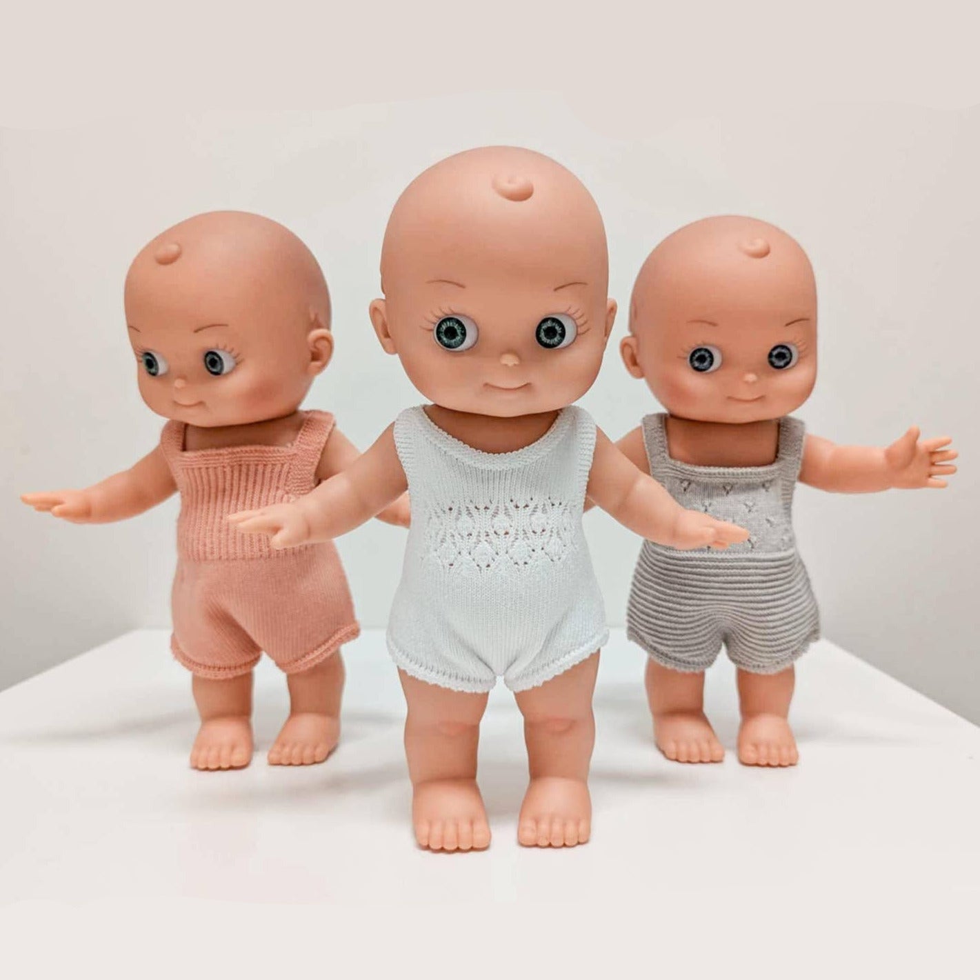 Three dolls in different outfits on a white surface with a light gray background