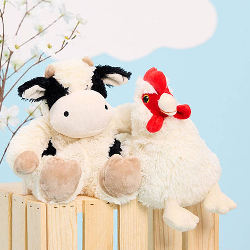Plush cow and rooster sitting on a wooden fence with a light blue background